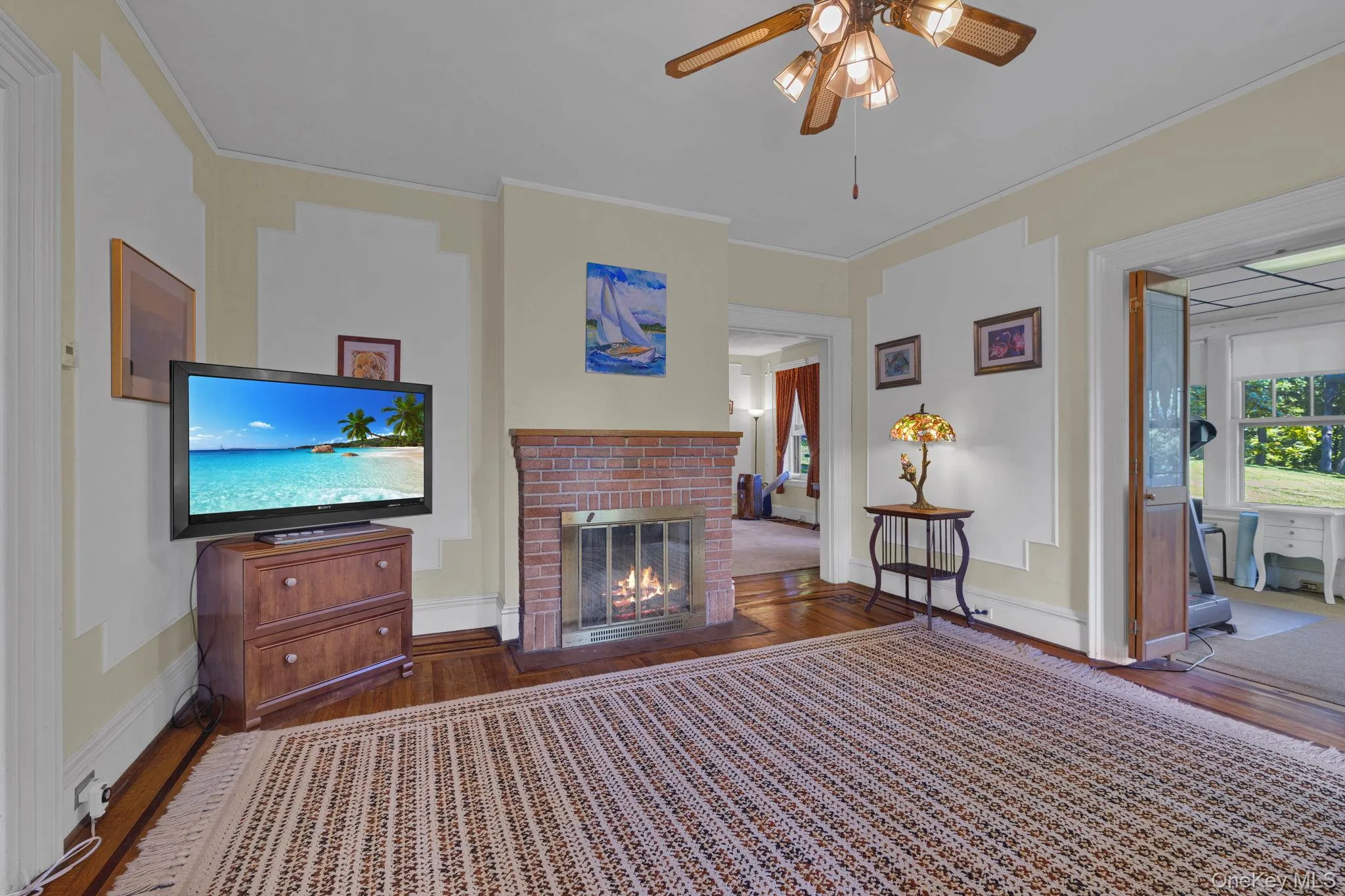Living area with dark wood-type flooring, crown molding, ceiling fan, and a fireplace Living area with dark wood-type flooring, crown molding, ceiling fan, and a fireplace