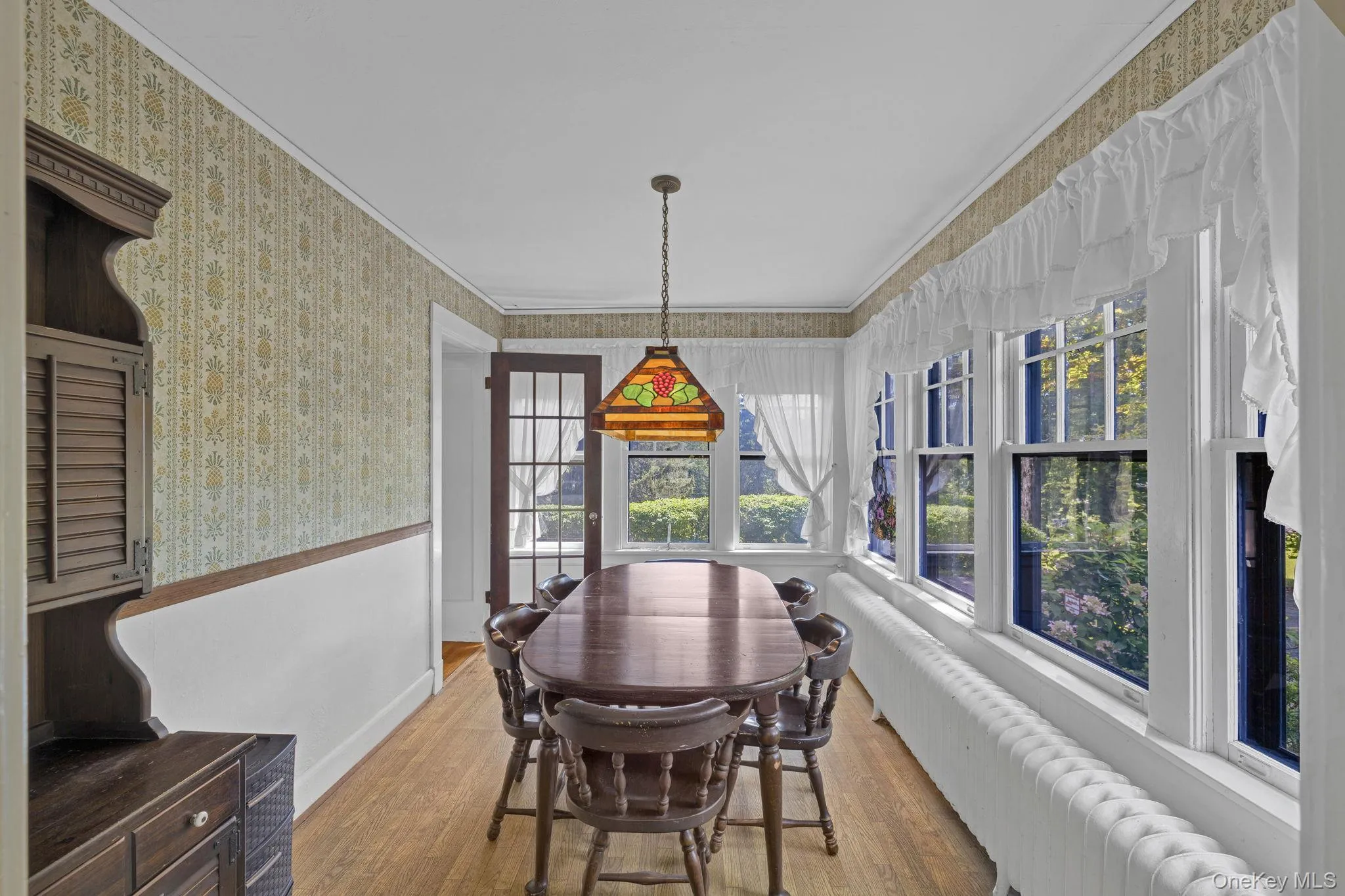 Dining space with wood finished floors, wallpapered walls, ornamental molding, radiator heating unit, and wainscoting Dining space with wood finished floors, wallpapered walls, ornamental molding, radiator heating unit, and wainscoting