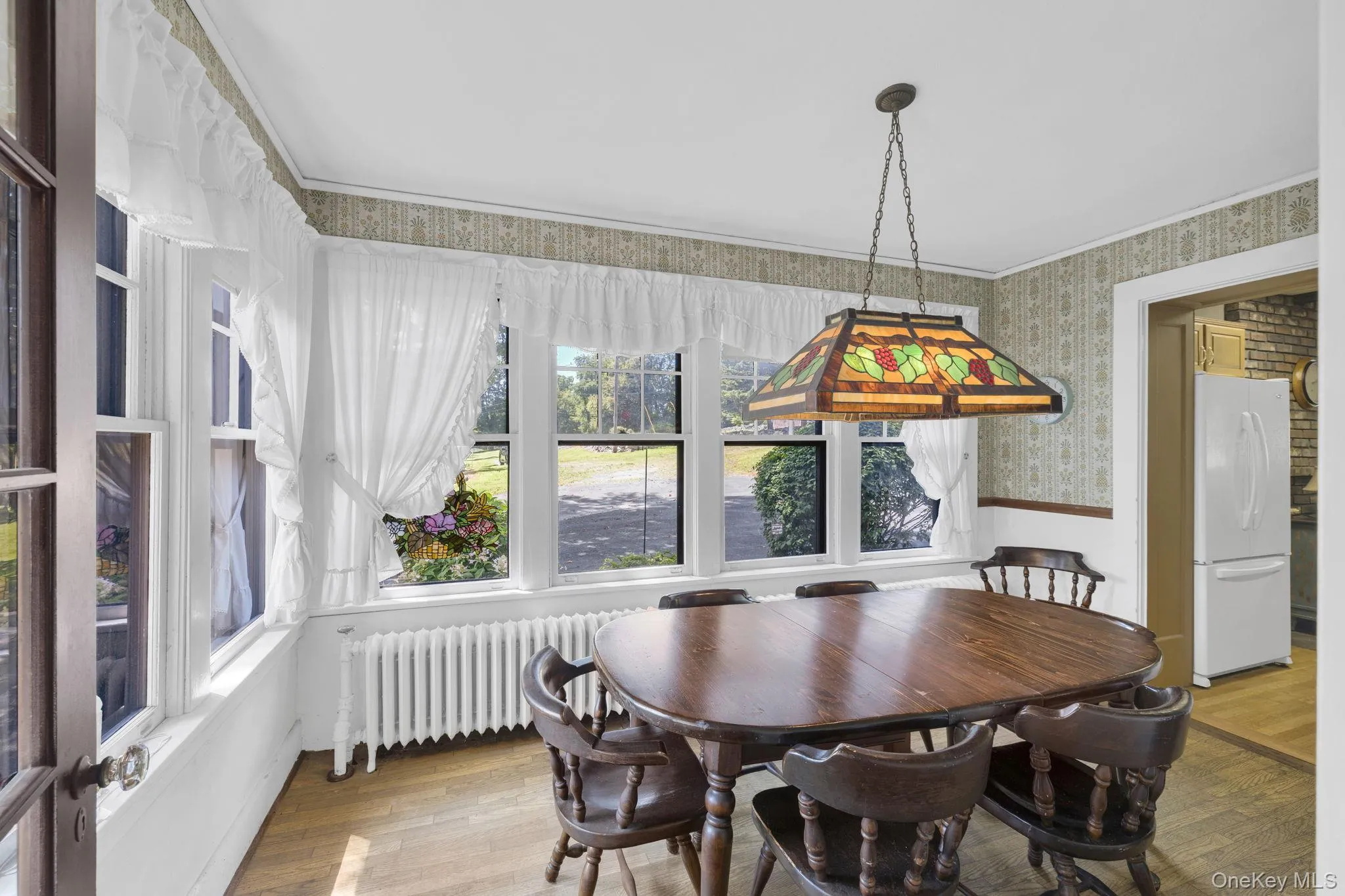 Dining room featuring radiator heating unit, light wood-type flooring, wallpapered walls, crown molding, and a wainscoted wall Dining room featuring radiator heating unit, light wood-type flooring, wallpapered walls, crown molding, and a wainscoted wall
