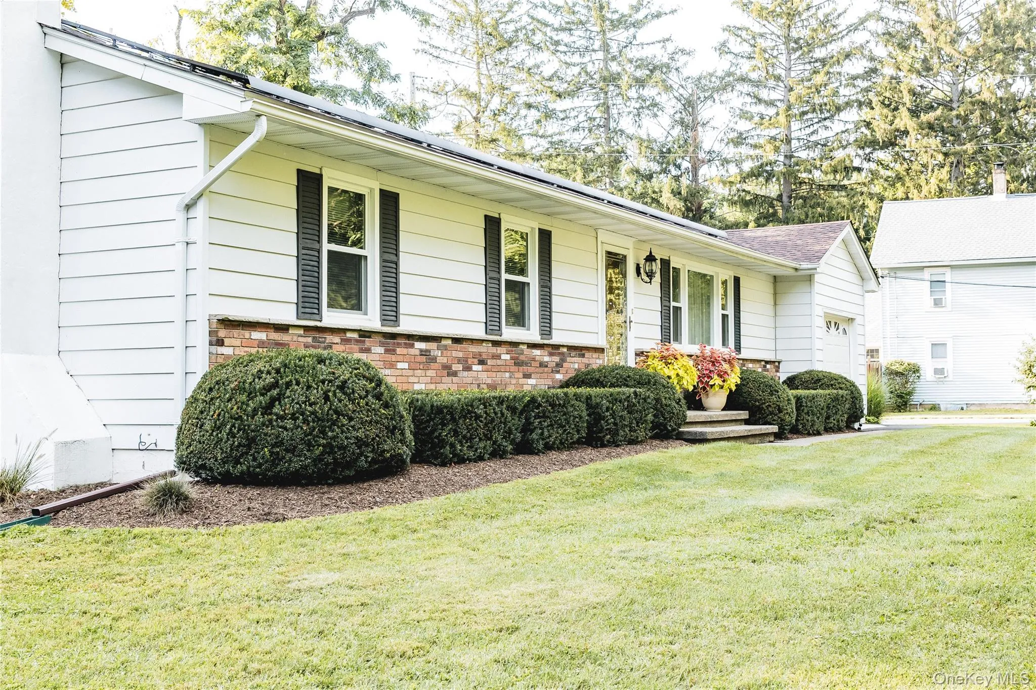 White horizontal siding exterior with lower brick, black window shutters, and a well-maintained lawn White horizontal siding exterior with lower brick, black window shutters, and a well-maintained lawn