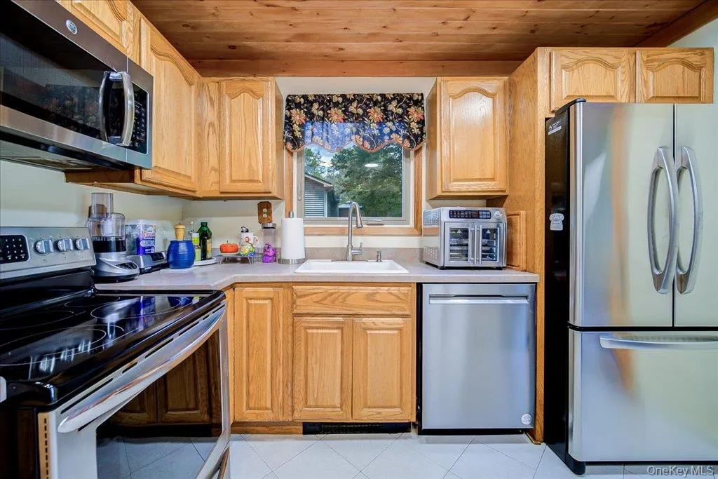 Wood-paneled ceiling, light wood-finish cabinetry, stainless steel appliances, and a white sink Wood-paneled ceiling, light wood-finish cabinetry, stainless steel appliances, and a white sink