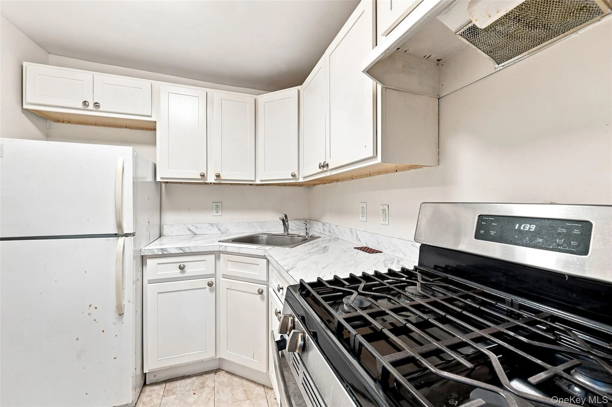 White cabinetry, stainless steel range, exhaust hood, corner sink, and a refrigerator White cabinetry, stainless steel range, exhaust hood, corner sink, and a refrigerator