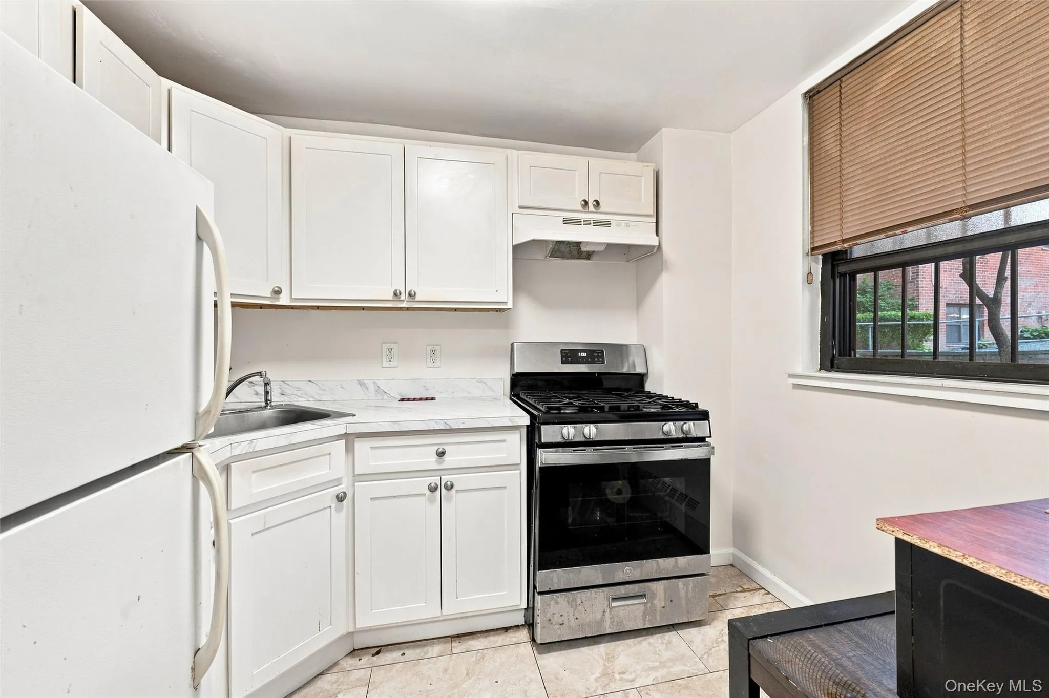 Kitchen featuring white cabinetry, stainless steel range, a window with window treatments, and tile flooring Kitchen featuring white cabinetry, stainless steel range, a window with window treatments, and tile flooring