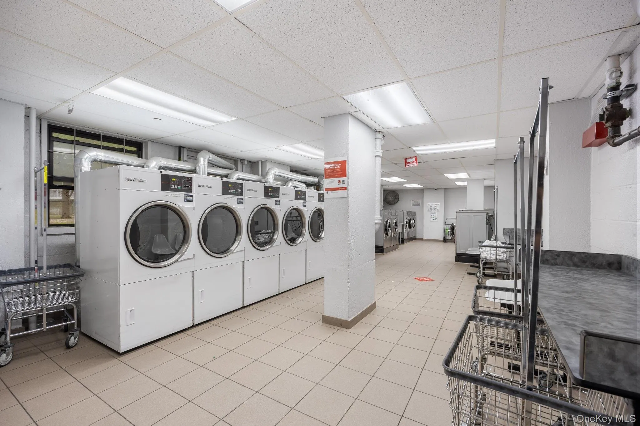 Communal laundry facility featuring multiple front-load washers and dryers, tiled flooring, and ample counter space Communal laundry facility featuring multiple front-load washers and dryers, tiled flooring, and ample counter space