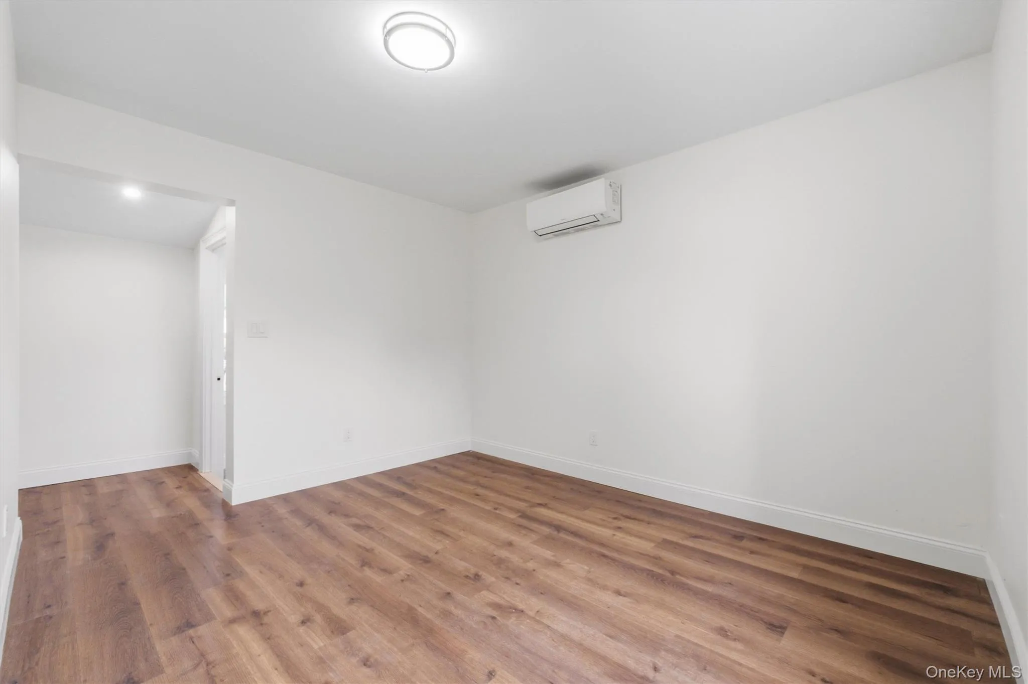 Wood-finish flooring, white walls, and a wall-mounted climate control unit Wood-finish flooring, white walls, and a wall-mounted climate control unit