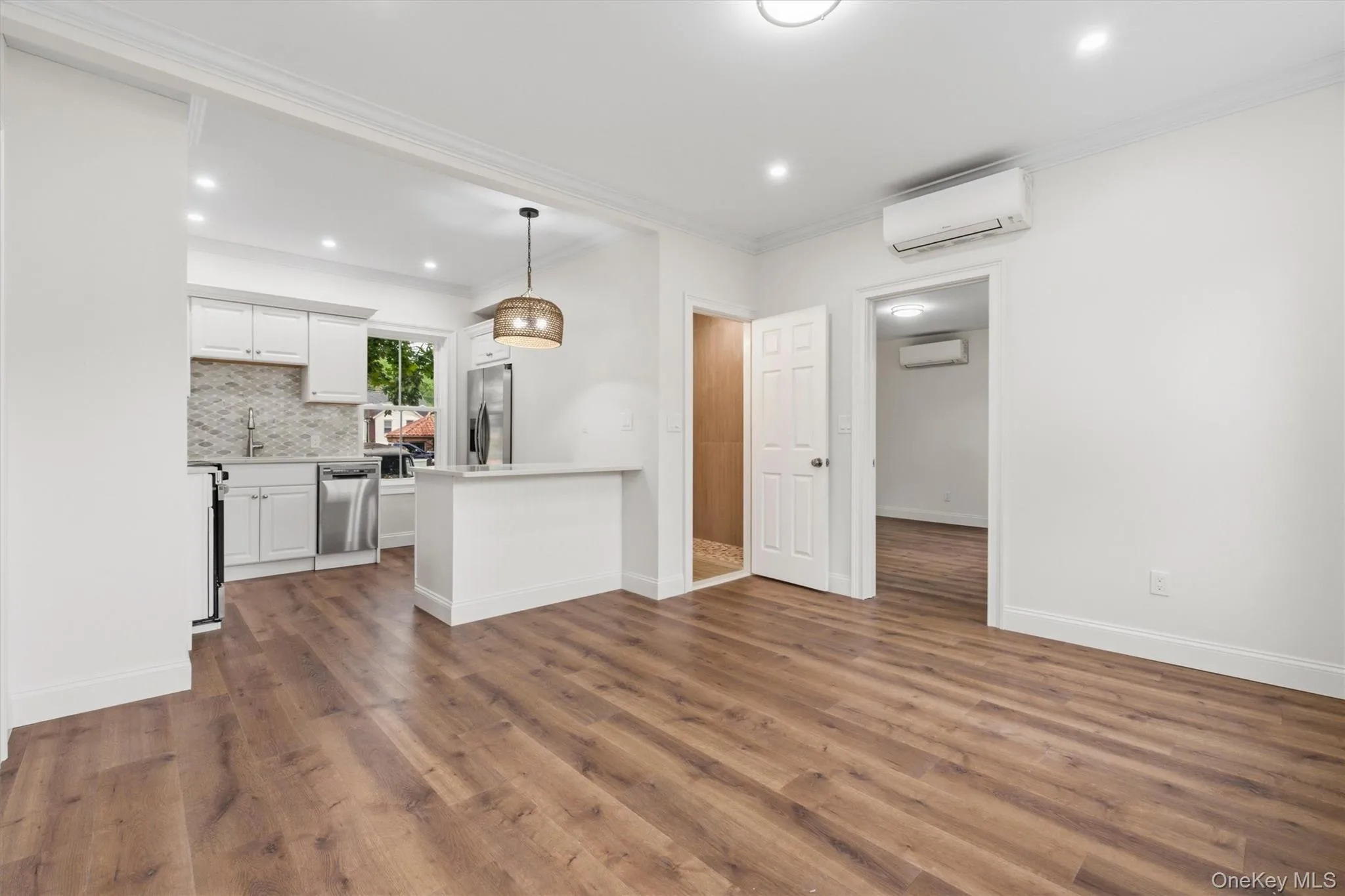 Open-concept living area with wood-finish flooring, recessed lighting, crown molding, and a split-system air conditioning unit Open-concept living area with wood-finish flooring, recessed lighting, crown molding, and a split-system air conditioning unit