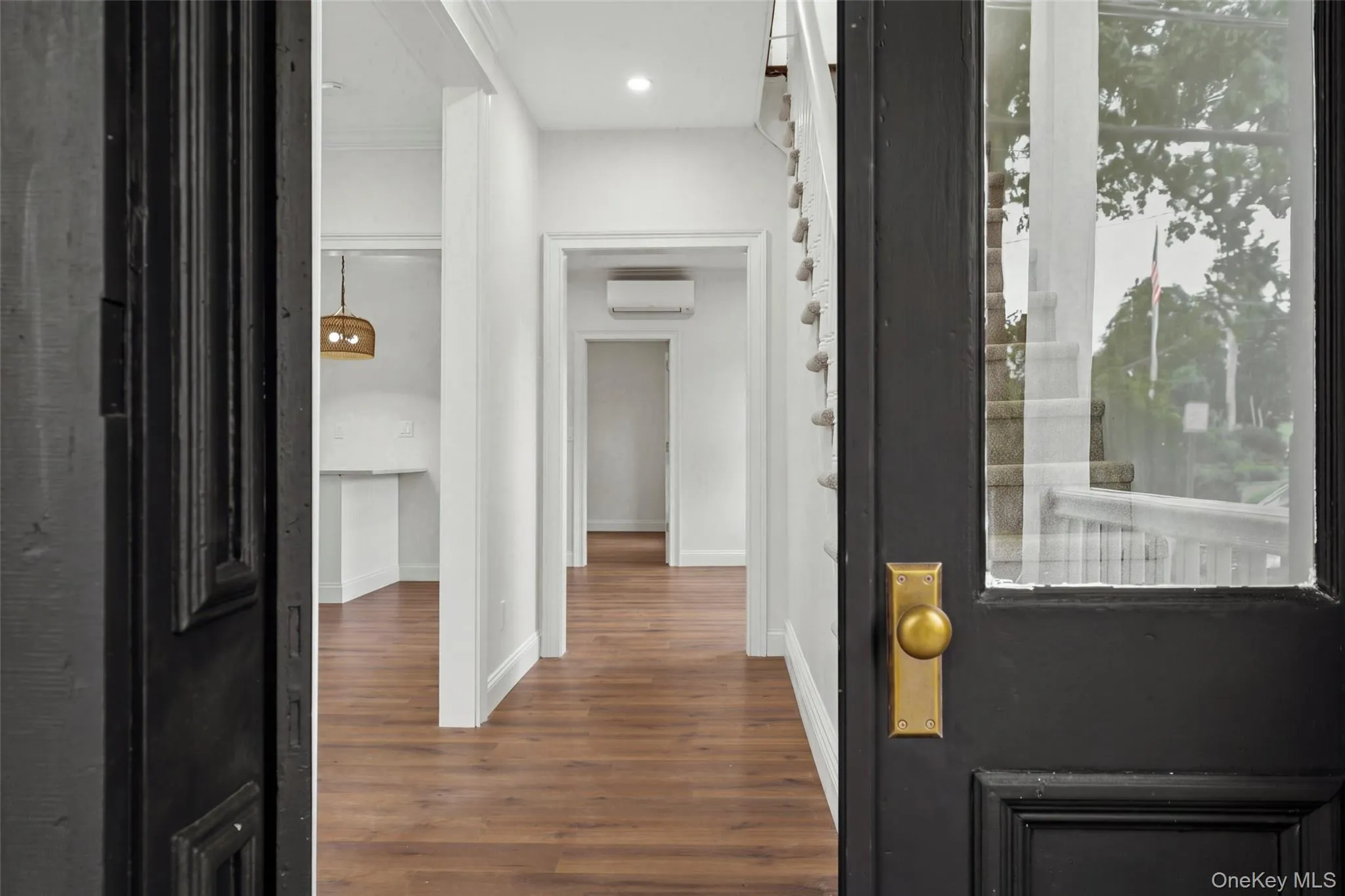 Entryway with wood-finish flooring, white walls, recessed lighting, and a dark paneled door with brass hardware Entryway with wood-finish flooring, white walls, recessed lighting, and a dark paneled door with brass hardware