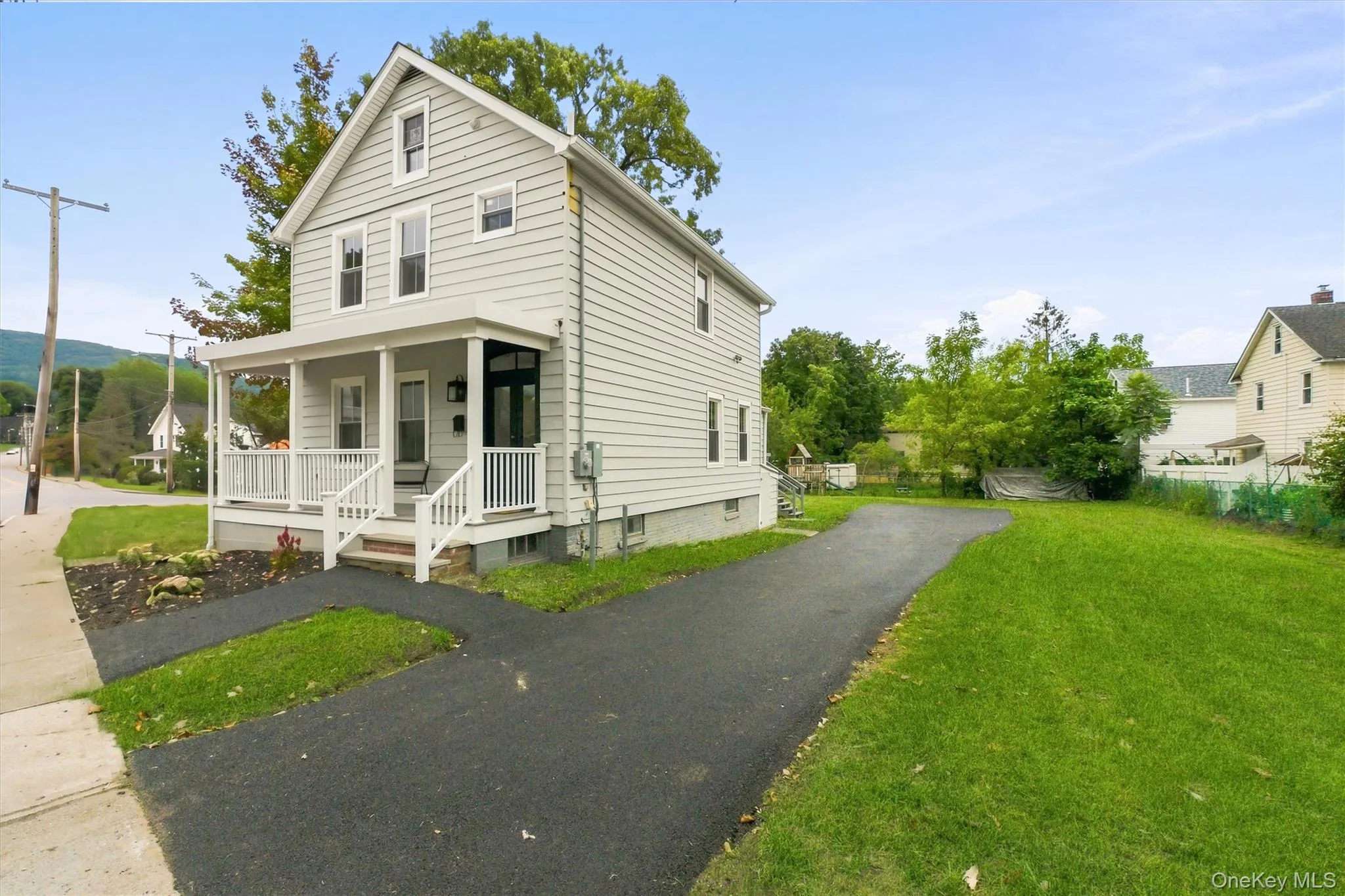 Two-story residence with light gray siding, a covered front porch, a paved driveway, and a spacious grassy yard Two-story residence with light gray siding, a covered front porch, a paved driveway, and a spacious grassy yard