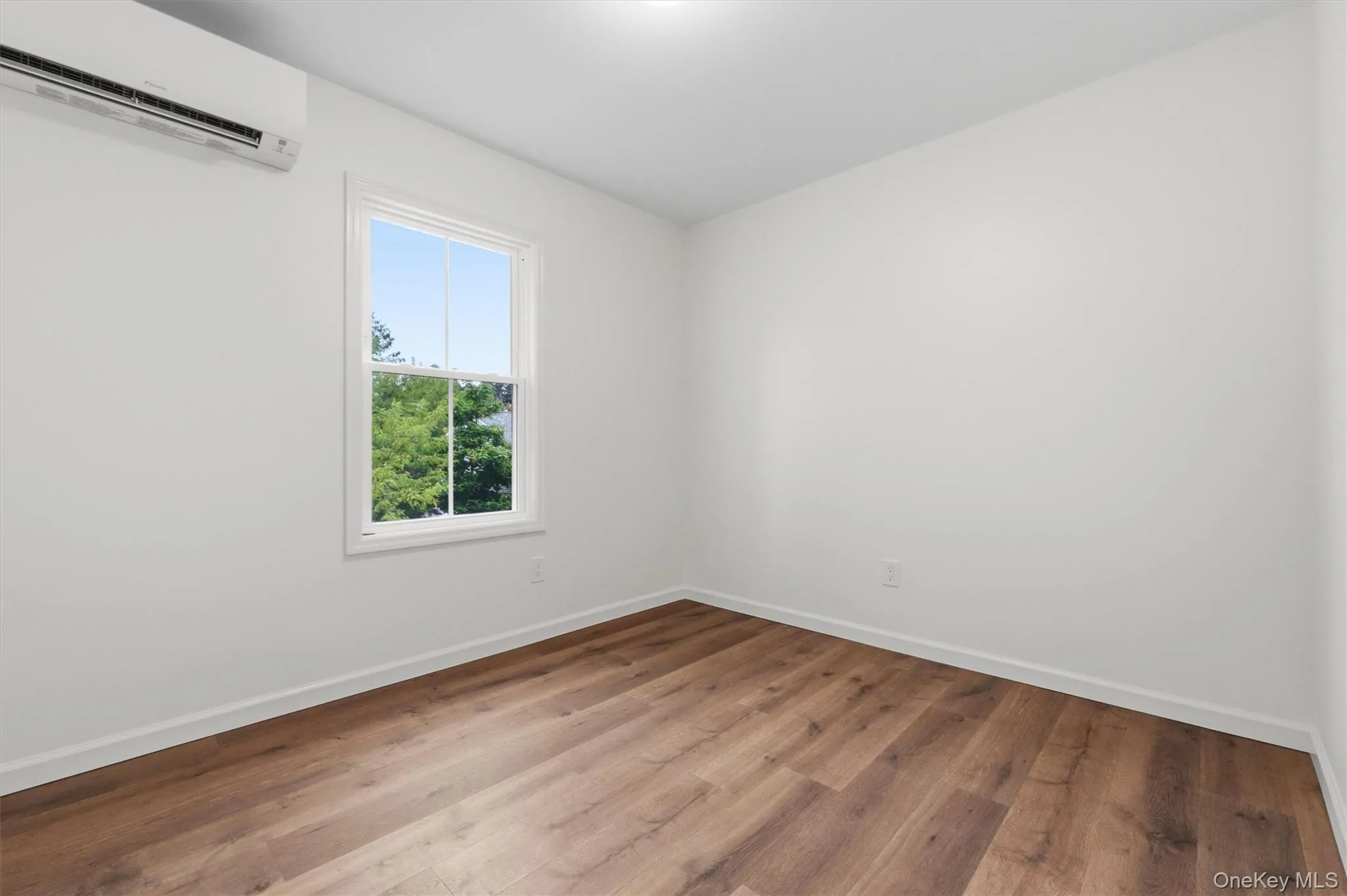 White walls, wood-finish flooring, single window, and a wall-mounted air conditioning unit White walls, wood-finish flooring, single window, and a wall-mounted air conditioning unit