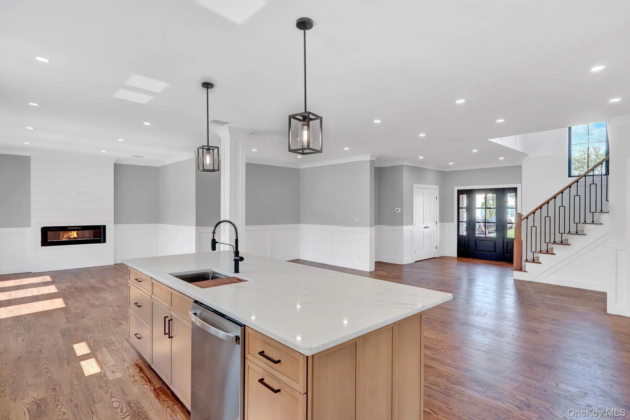 Open-concept main level featuring wood-finish flooring, a modern linear fireplace, and a kitchen island with a built-in sink and stainless steel dishwasher Open-concept main level featuring wood-finish flooring, a modern linear fireplace, and a kitchen island with a built-in sink and stainless steel dishwasher