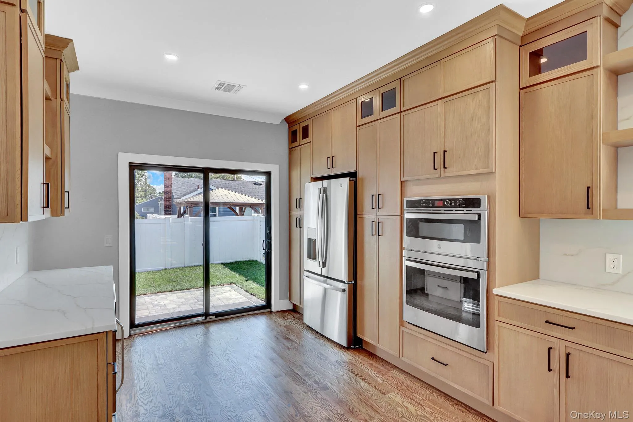 Hardwood flooring, light wood-finish cabinetry, stainless steel appliances, white countertops, and a sliding glass door to the exterior Hardwood flooring, light wood-finish cabinetry, stainless steel appliances, white countertops, and a sliding glass door to the exterior