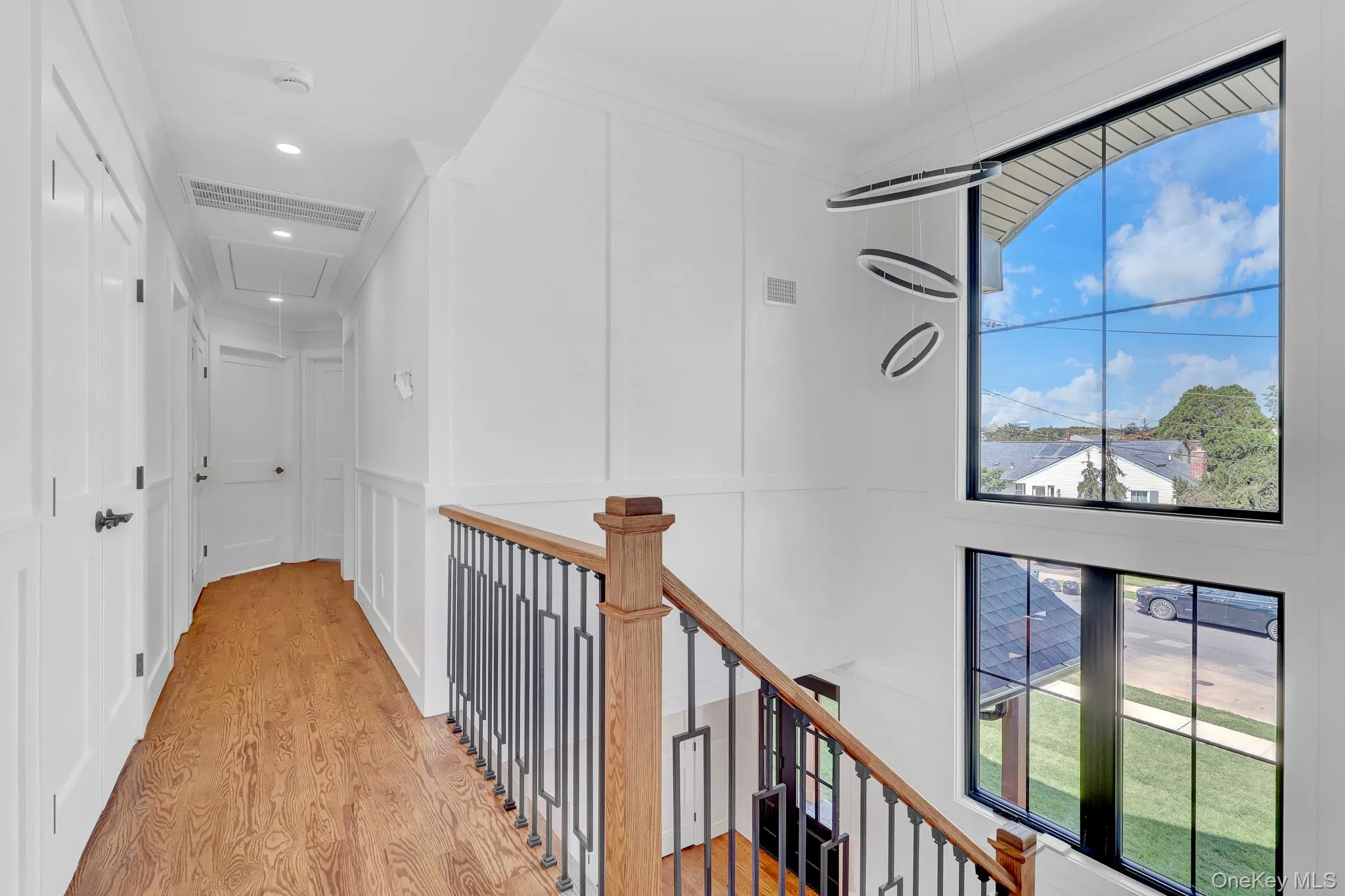Staircase featuring wood-finish handrail, wrought iron balusters, and a contemporary chandelier with double windows for natural light Staircase featuring wood-finish handrail, wrought iron balusters, and a contemporary chandelier with double windows for natural light