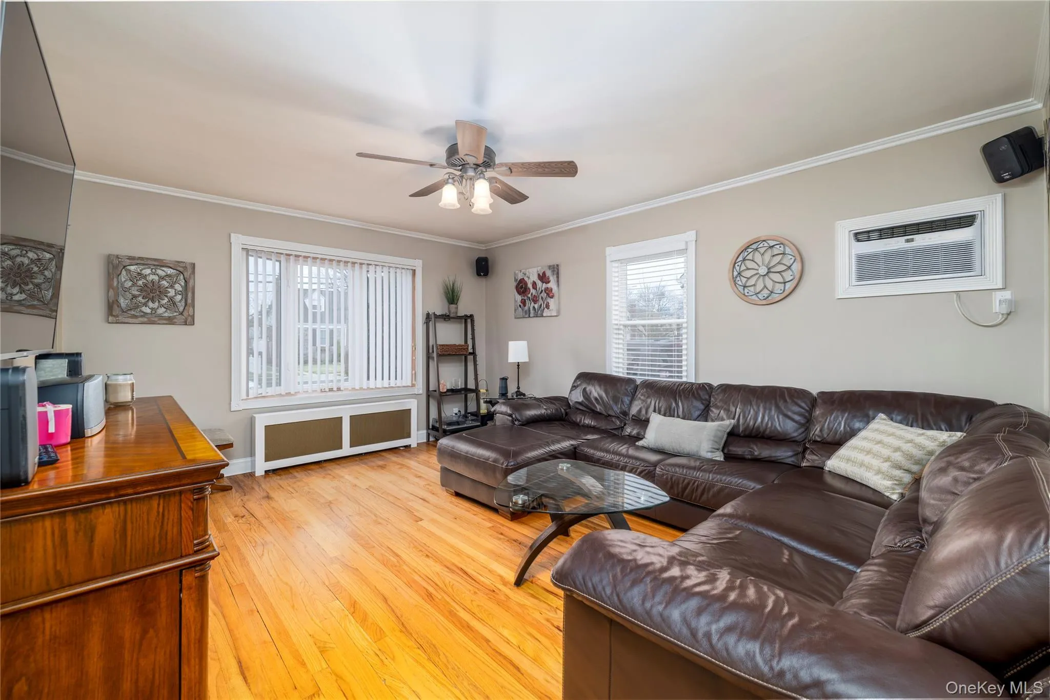Living area featuring crown molding, light wood finished floors, radiator heating unit, a ceiling fan, and an AC wall unit Living area featuring crown molding, light wood finished floors, radiator heating unit, a ceiling fan, and an AC wall unit