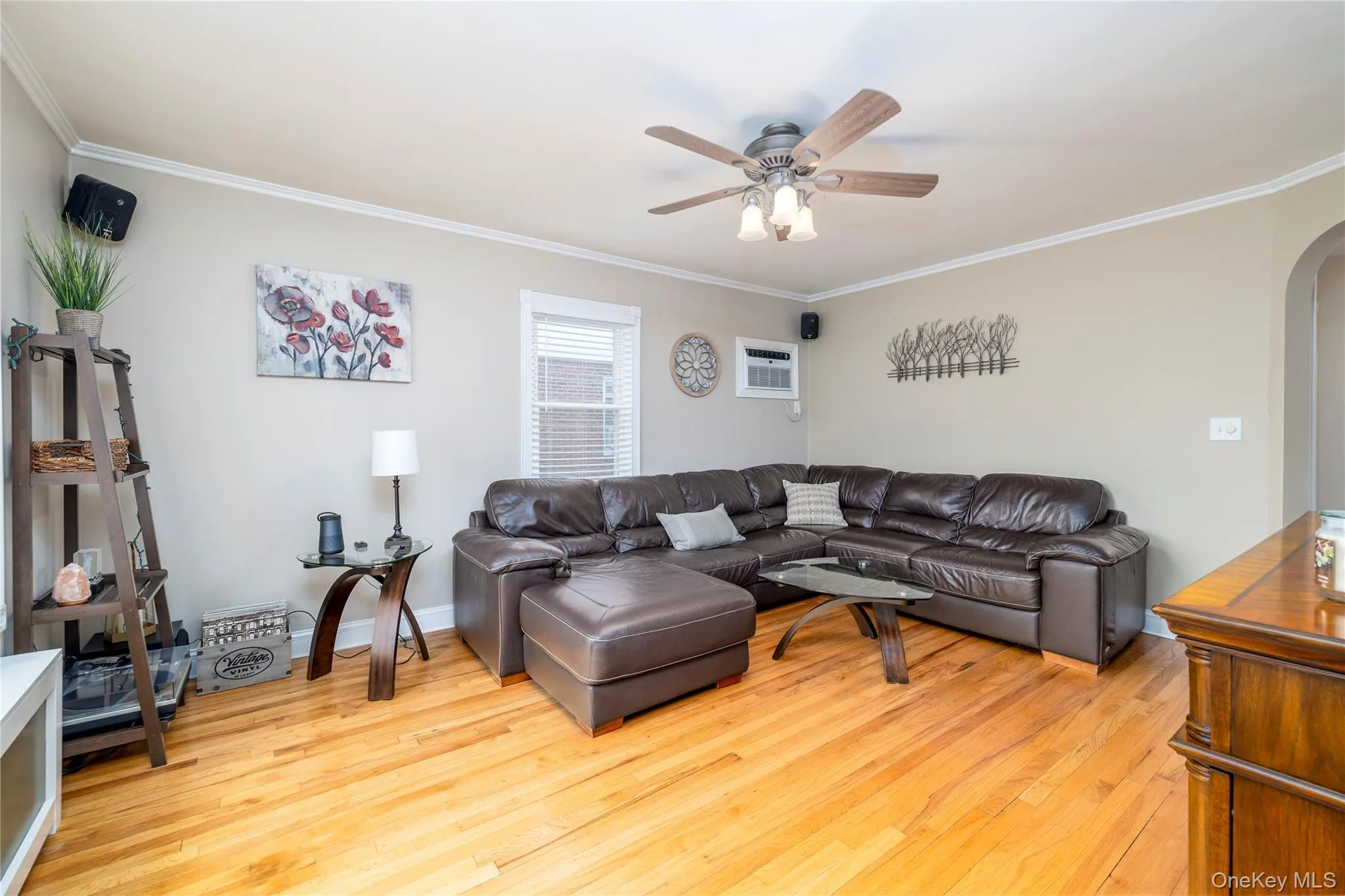 Living room featuring a wall unit AC, ornamental molding, arched walkways, light wood-style floors, and ceiling fan Living room featuring a wall unit AC, ornamental molding, arched walkways, light wood-style floors, and ceiling fan