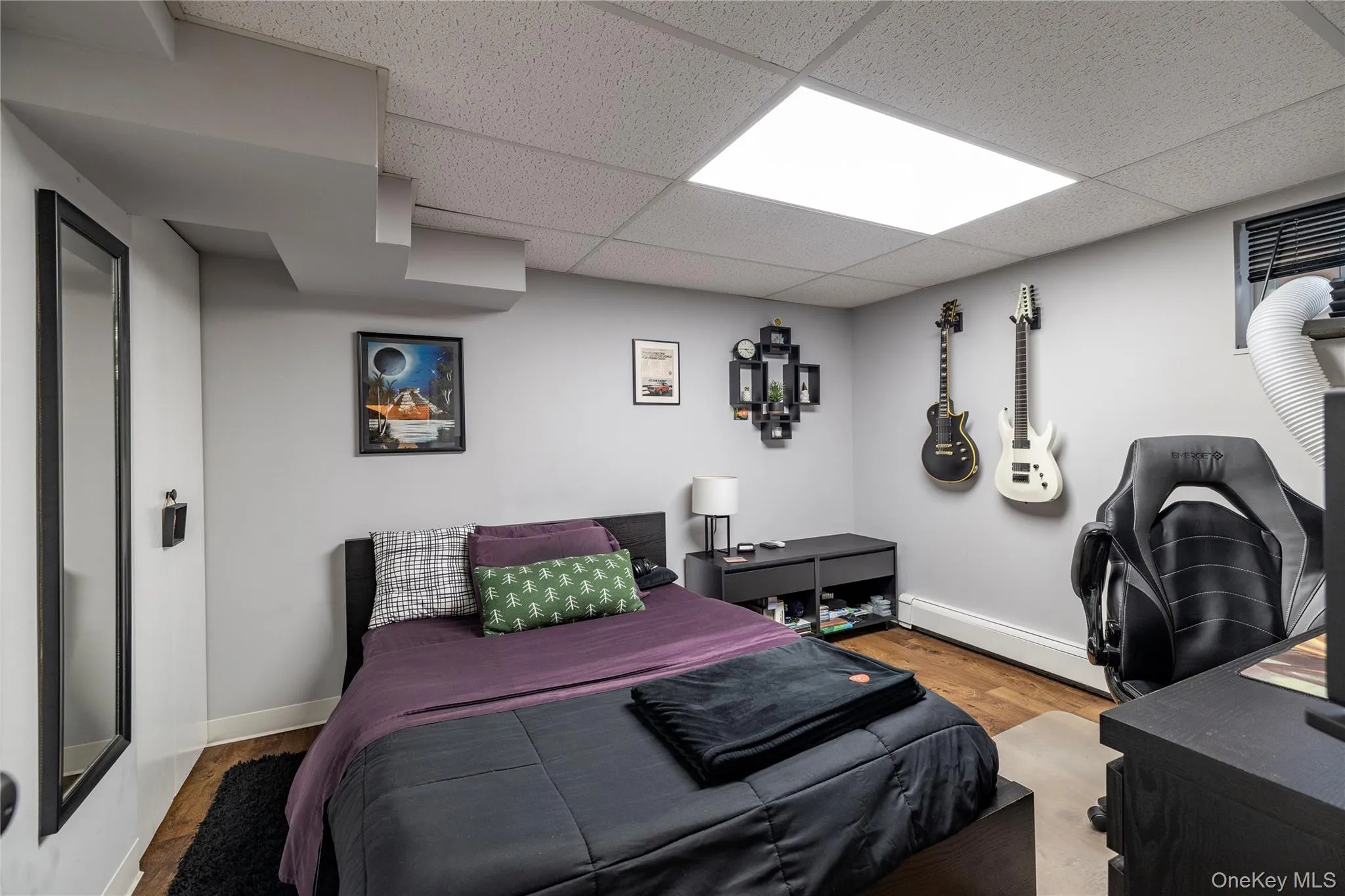 Bedroom with baseboards, wood finished floors, a paneled ceiling, and baseboard heating Bedroom with baseboards, wood finished floors, a paneled ceiling, and baseboard heating