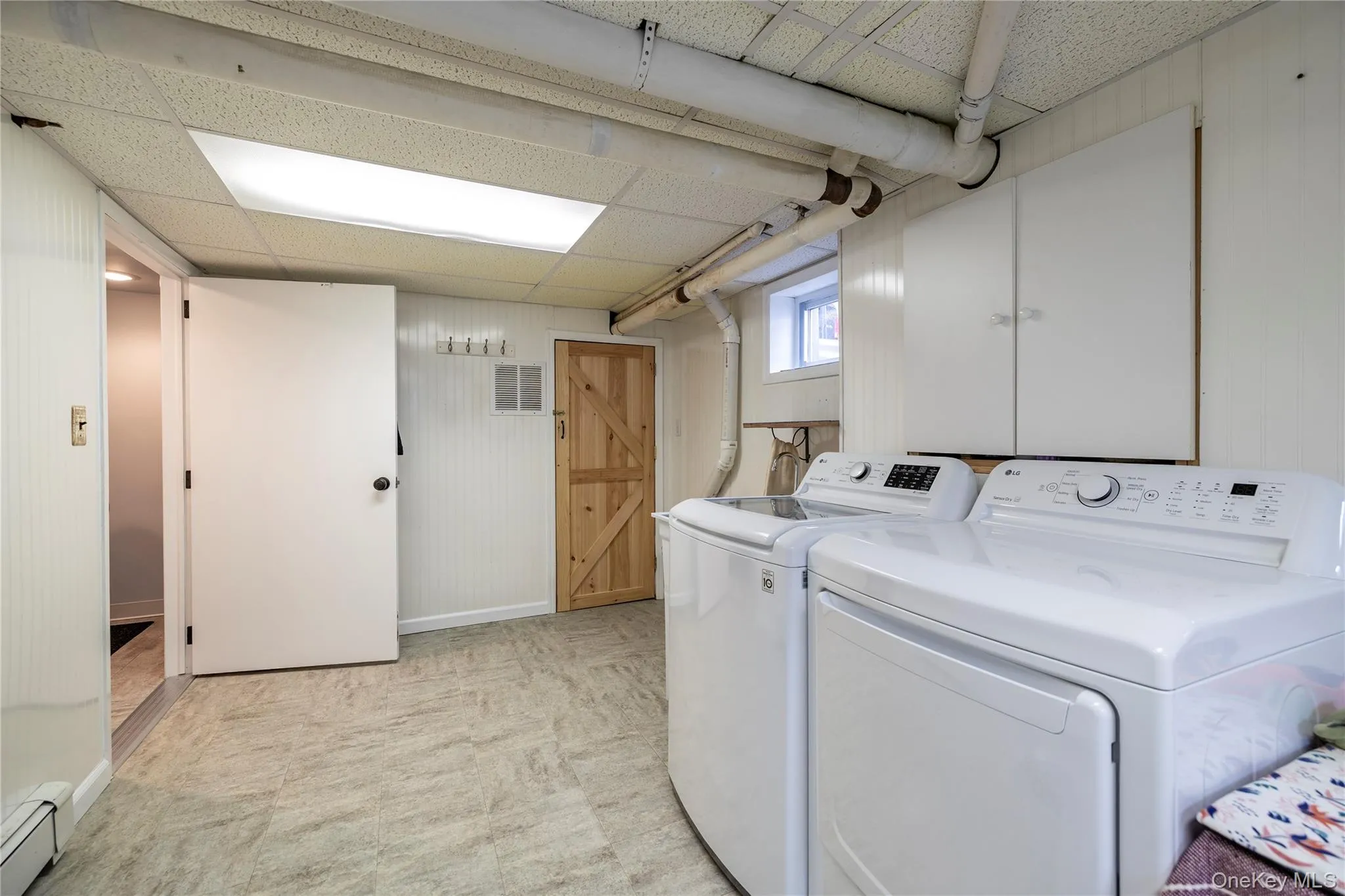Laundry area featuring wood walls, visible vents, a baseboard radiator, baseboards, and separate washer and dryer Laundry area featuring wood walls, visible vents, a baseboard radiator, baseboards, and separate washer and dryer