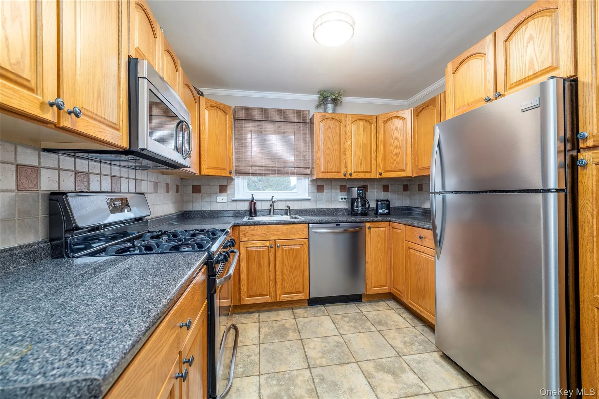 Kitchen featuring crown molding, a sink, tasteful backsplash, appliances with stainless steel finishes, and dark countertops Kitchen featuring crown molding, a sink, tasteful backsplash, appliances with stainless steel finishes, and dark countertops