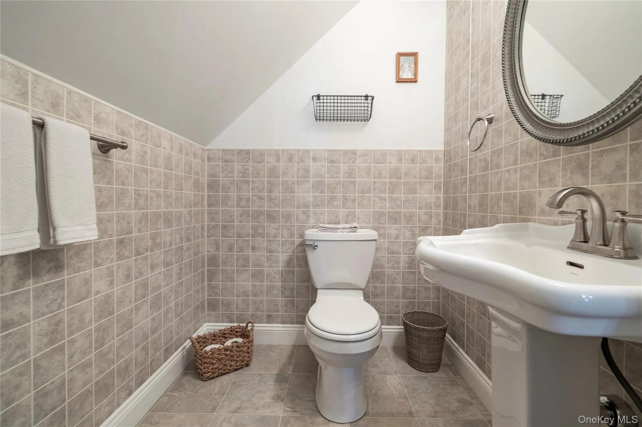 Half bath featuring tile patterned floors, vaulted ceiling, toilet, a sink, and tile walls Half bath featuring tile patterned floors, vaulted ceiling, toilet, a sink, and tile walls
