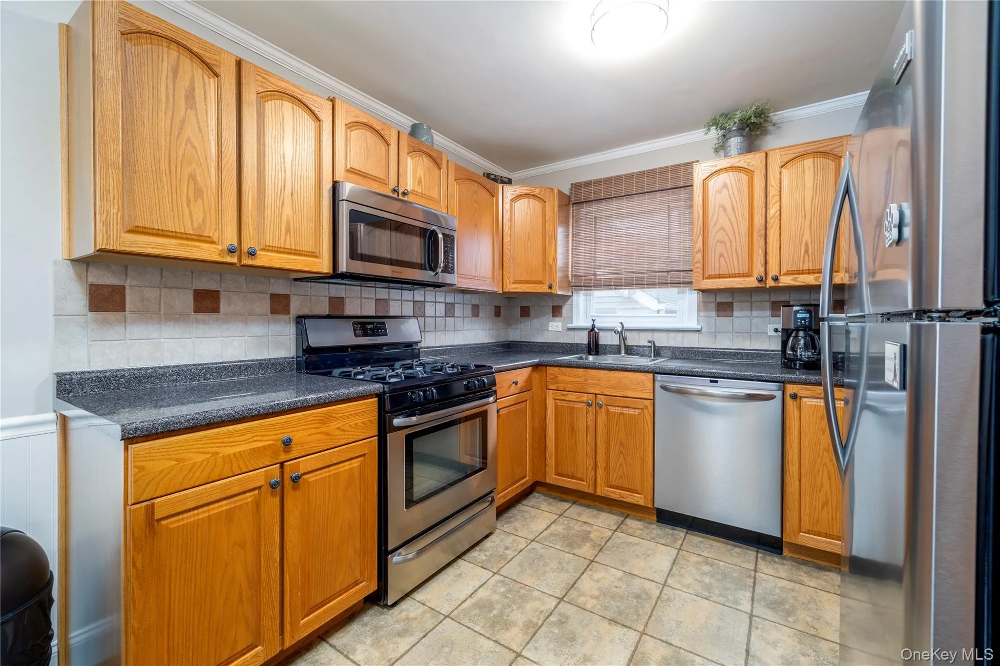 Kitchen featuring crown molding, light tile patterned floors, backsplash, a sink, and appliances with stainless steel finishes Kitchen featuring crown molding, light tile patterned floors, backsplash, a sink, and appliances with stainless steel finishes