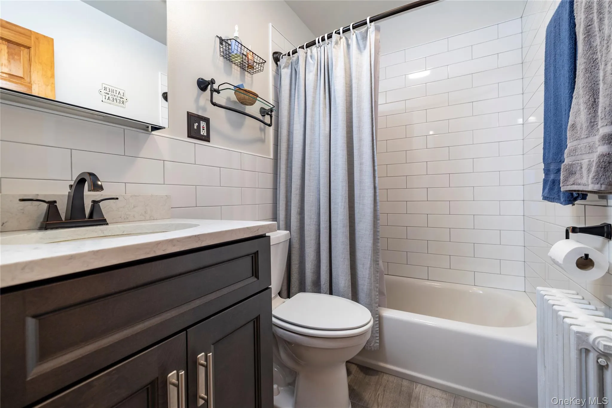 Full bathroom featuring vanity, tile walls, toilet, radiator heating unit, and wood finished floors Full bathroom featuring vanity, tile walls, toilet, radiator heating unit, and wood finished floors