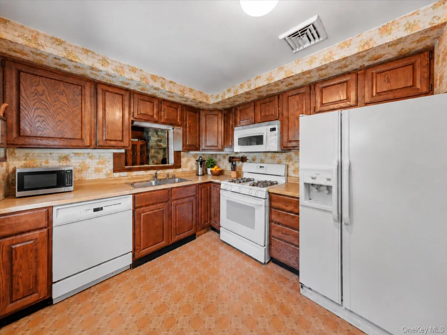 Full kitchen view featuring extensive wood cabinetry, ample counter space, and a practical appliance layout. Full kitchen view featuring extensive wood cabinetry, ample counter space, and a practical appliance layout.