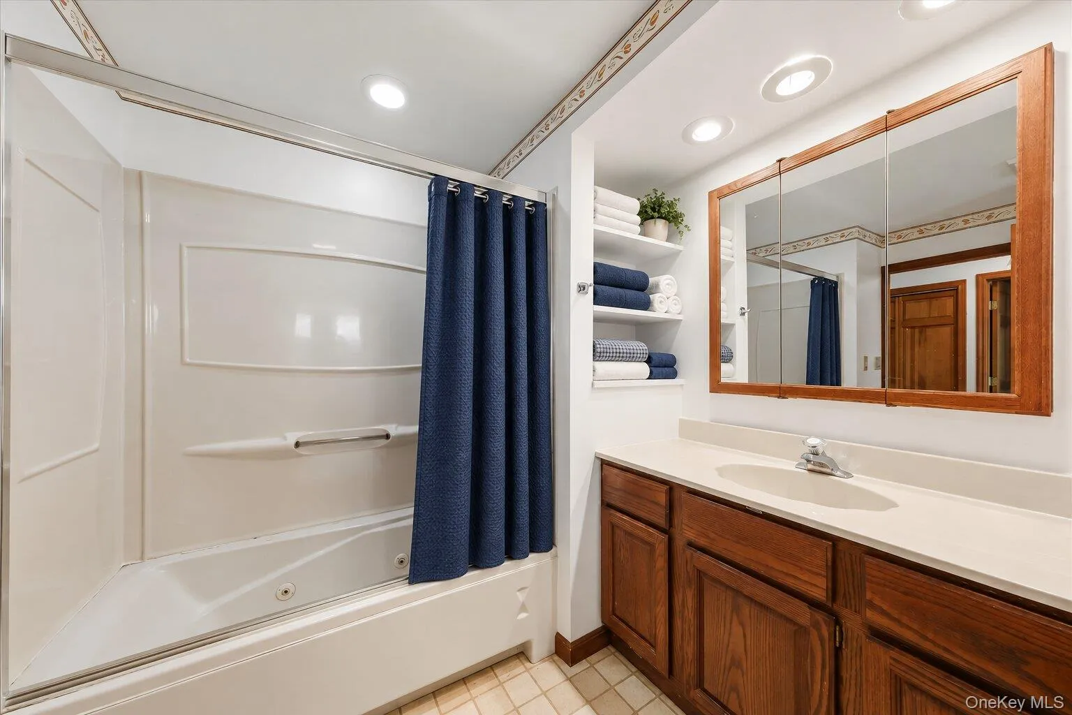 Full bathroom featuring a tub/shower combination, spacious vanity, built-in shelving, and generous mirror space. Full bathroom featuring a tub/shower combination, spacious vanity, built-in shelving, and generous mirror space.