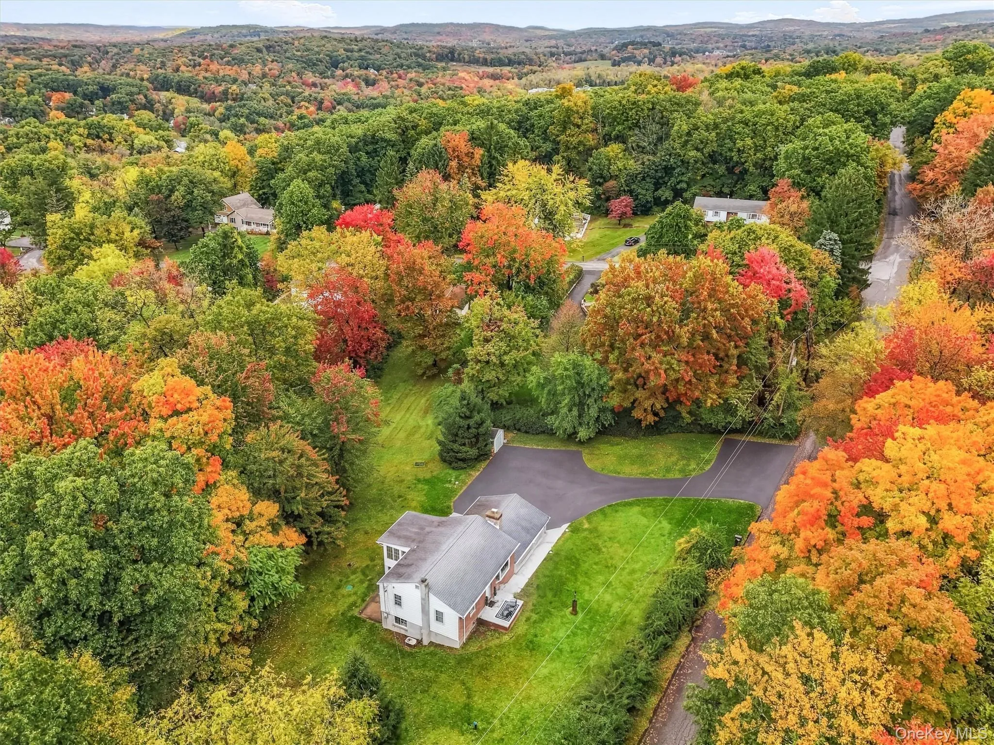 Elevated aerial view showcasing the home, spacious driveway, green lawn, and surrounding mature trees displaying vibrant autumn colors. Elevated aerial view showcasing the home, spacious driveway, green lawn, and surrounding mature trees displaying vibrant autumn colors.