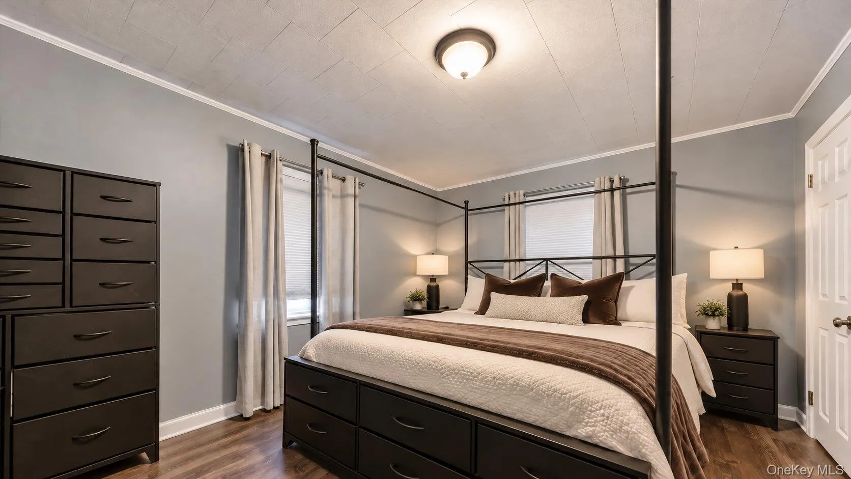 Virtually staged bedding and decluttered. Bedroom featuring gray walls, wood-look flooring, two windows, a four-poster bed with built-in drawer storage, and matching bedroom furniture. Virtually staged bedding and decluttered. Bedroom featuring gray walls, wood-look flooring, two windows, a four-poster bed with built-in drawer storage, and matching bedroom furniture.