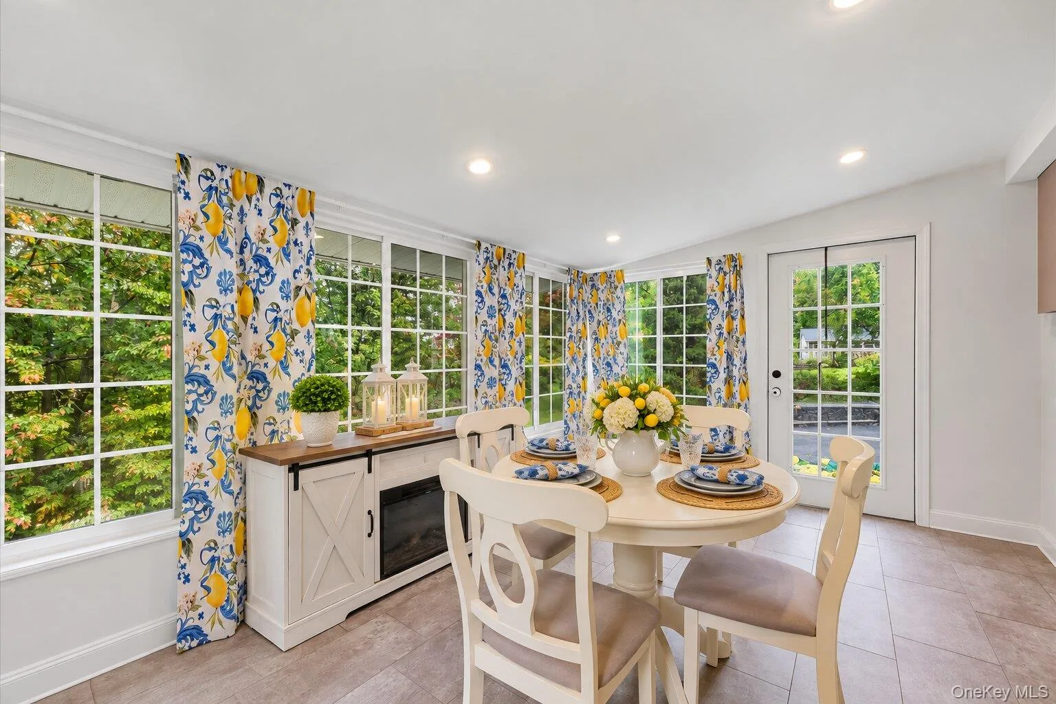 Virtually decluttered and the table has been set. Dining area surrounded by large windows with colorful patterned curtains, tile flooring, and a round table with seating for four. Virtually decluttered and the table has been set. Dining area surrounded by large windows with colorful patterned curtains, tile flooring, and a round table with seating for four.
