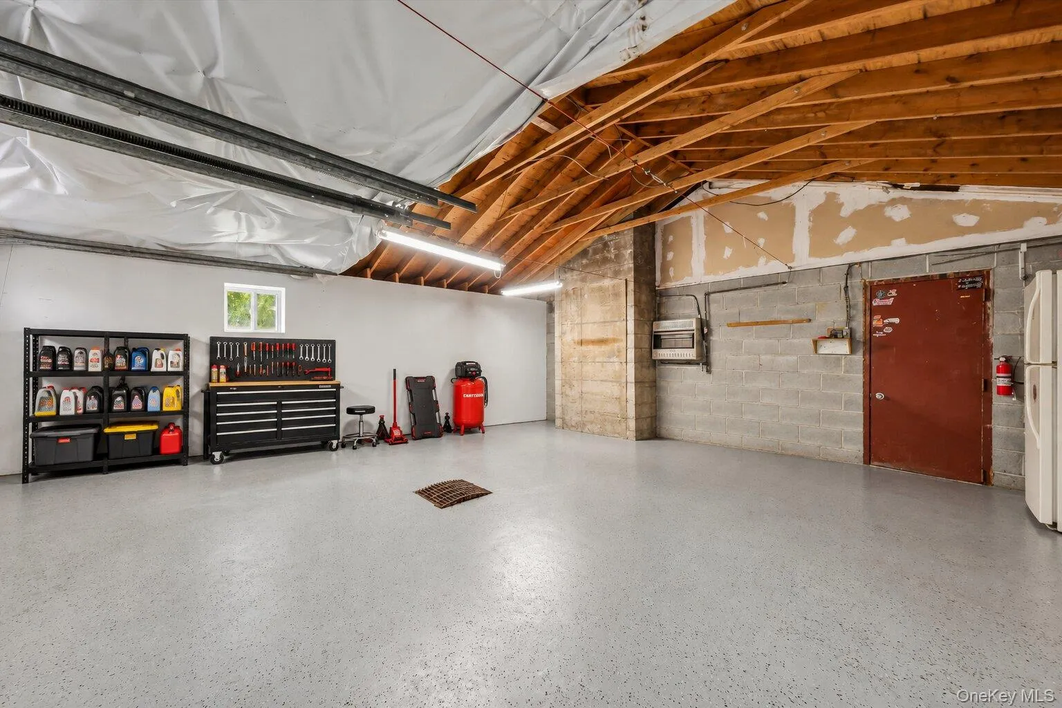 Virtually staged tools and decluttered. Additional garage view highlighting the open floor space, exposed wood rafters, utility storage shelves, tool chest, and workshop area. Virtually staged tools and decluttered. Additional garage view highlighting the open floor space, exposed wood rafters, utility storage shelves, tool chest, and workshop area.