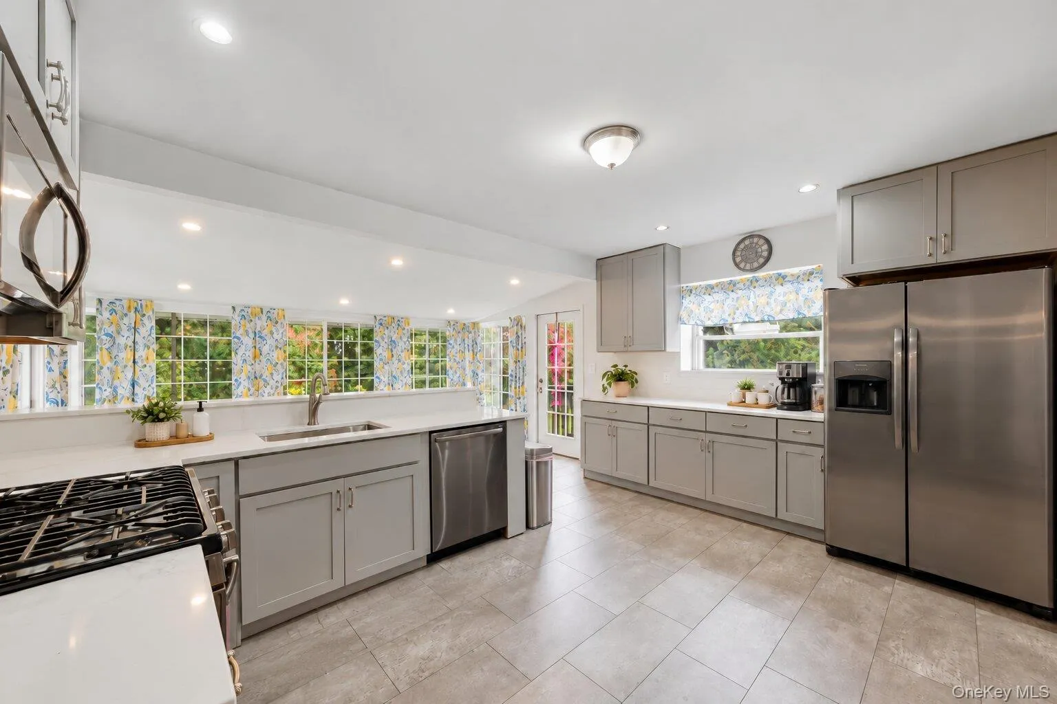 Virtually decluttered. Kitchen featuring gray cabinetry, white countertops, stainless steel appliances, tile flooring, and a sink overlooking multiple windows. Virtually decluttered. Kitchen featuring gray cabinetry, white countertops, stainless steel appliances, tile flooring, and a sink overlooking multiple windows.