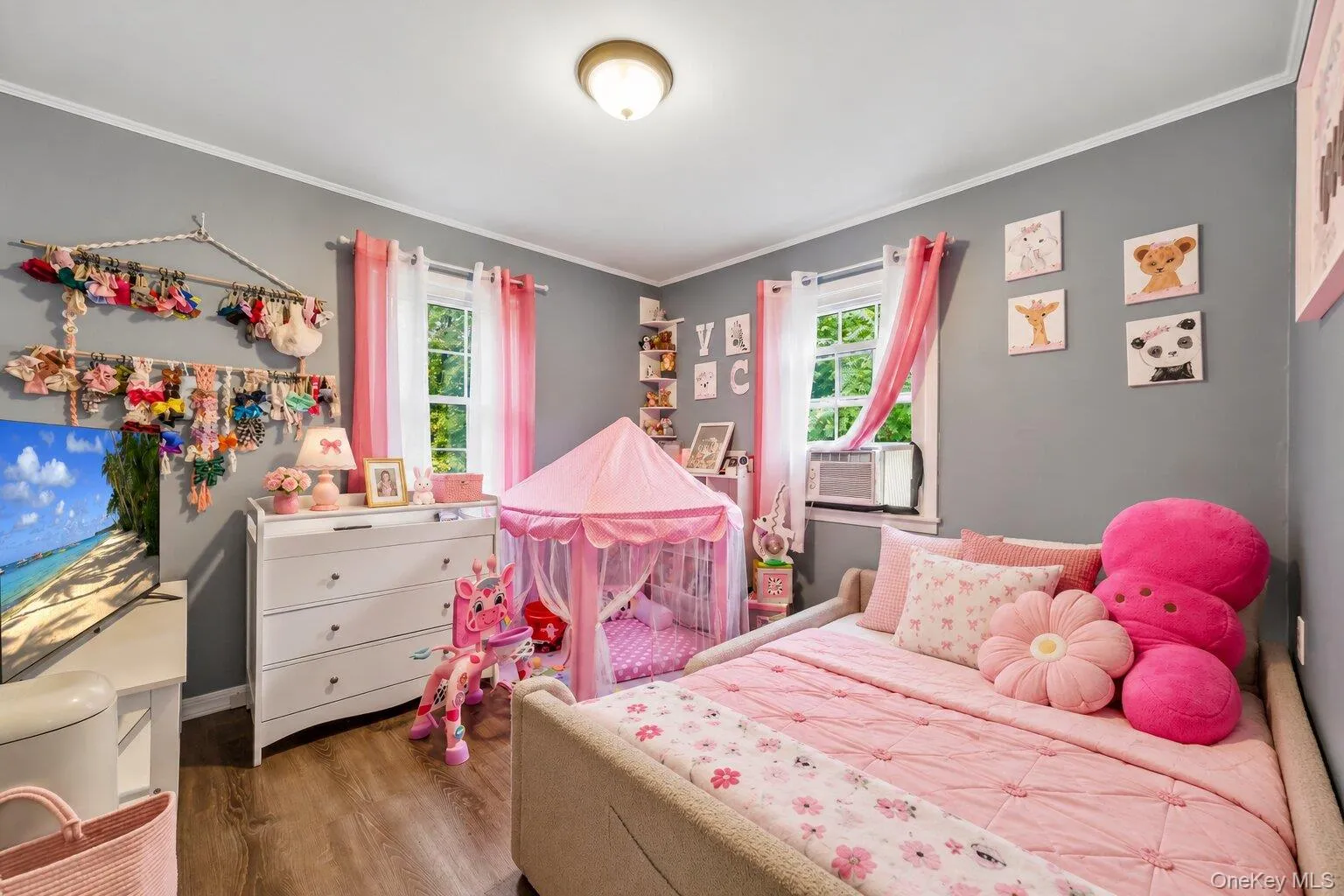 Virtually staged bedding and decluttered. Bedroom featuring gray walls, wood-look flooring, two windows, pink furnishings, a bed, dresser, and window air-conditioning unit. Virtually staged bedding and decluttered. Bedroom featuring gray walls, wood-look flooring, two windows, pink furnishings, a bed, dresser, and window air-conditioning unit.