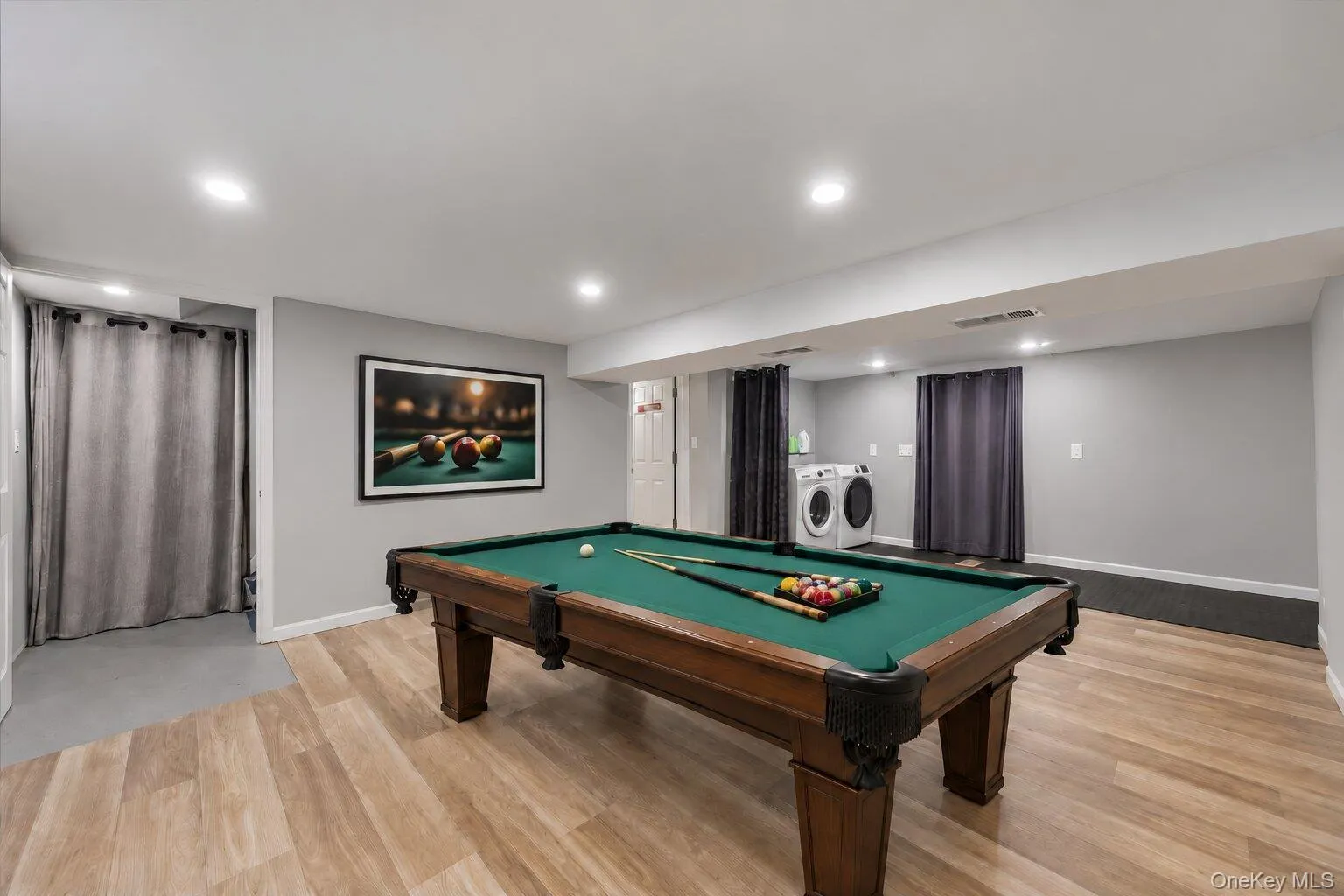 Virtually staged and decluttered recreation room featuring a billiards table, wood-look flooring, recessed lighting, and an adjoining laundry area. Virtually staged and decluttered recreation room featuring a billiards table, wood-look flooring, recessed lighting, and an adjoining laundry area.