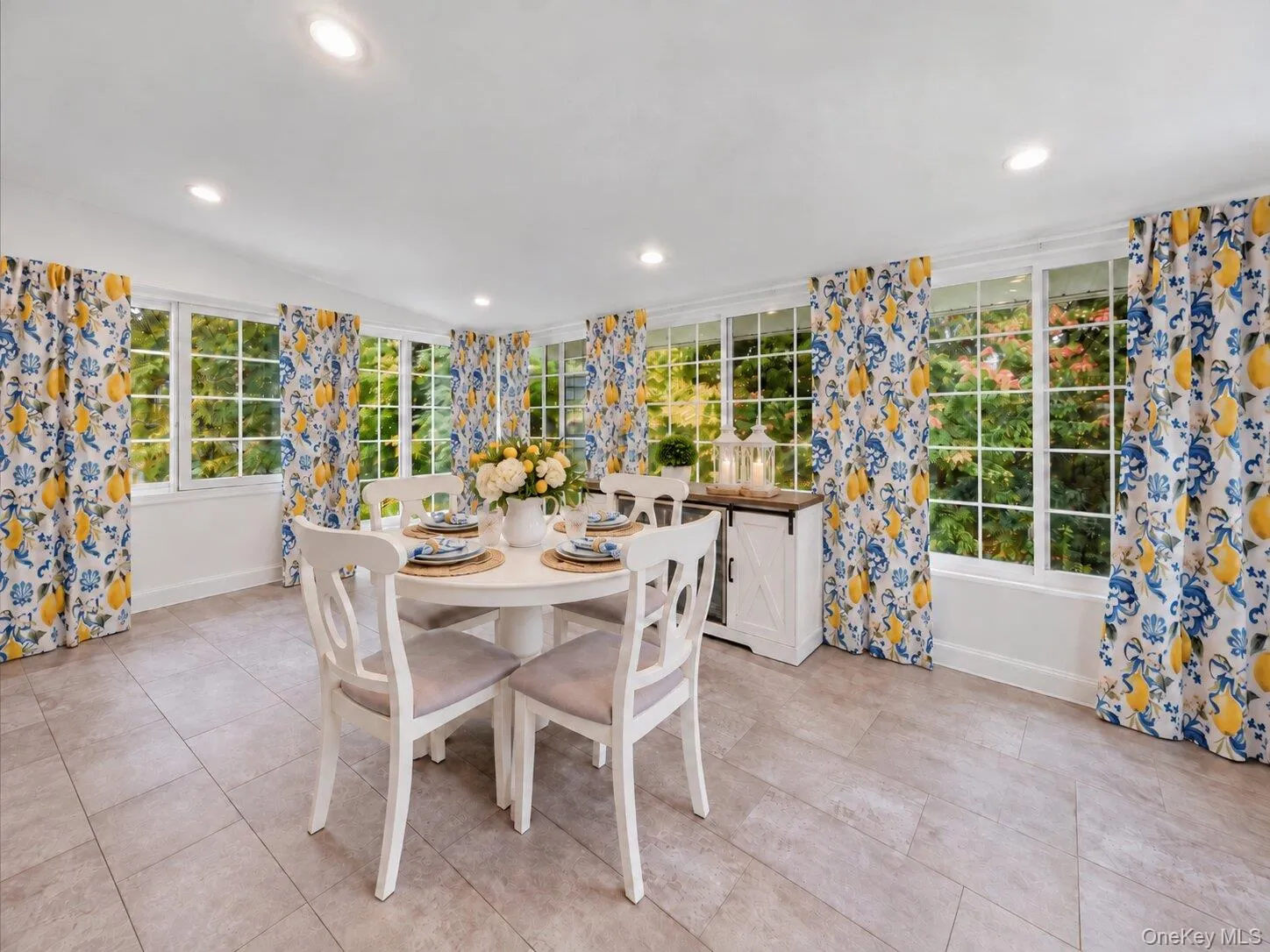 Virtually decluttered and the table has been set. Bright dining area featuring windows on multiple walls, patterned curtains, tile flooring, and a round dining table with four chairs. Virtually decluttered and the table has been set. Bright dining area featuring windows on multiple walls, patterned curtains, tile flooring, and a round dining table with four chairs.