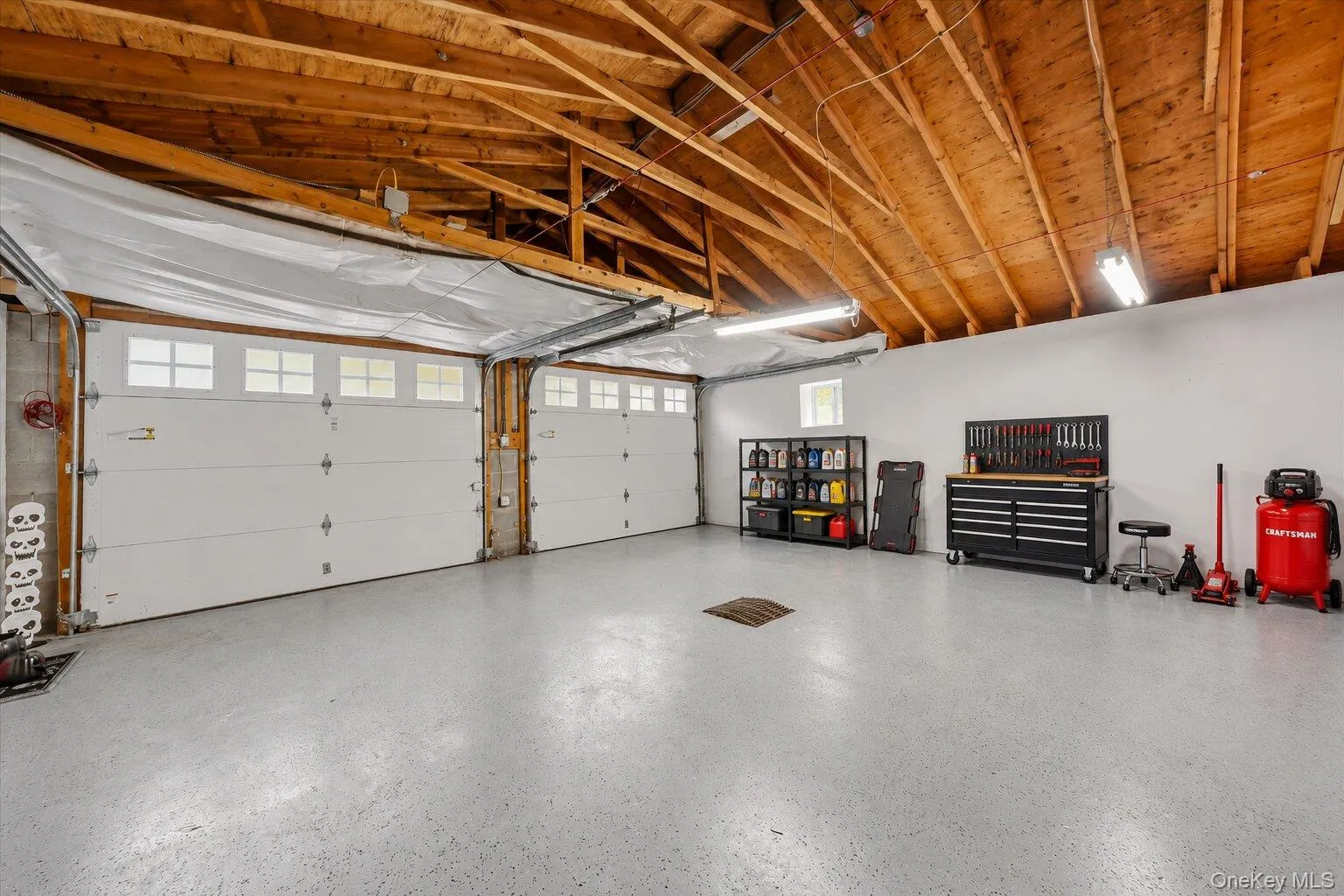 Virtually staged tools and decluttered. Spacious two-car garage featuring two overhead doors, a finished floor, exposed wood ceiling beams, and an organized tool and storage area. Virtually staged tools and decluttered. Spacious two-car garage featuring two overhead doors, a finished floor, exposed wood ceiling beams, and an organized tool and storage area.