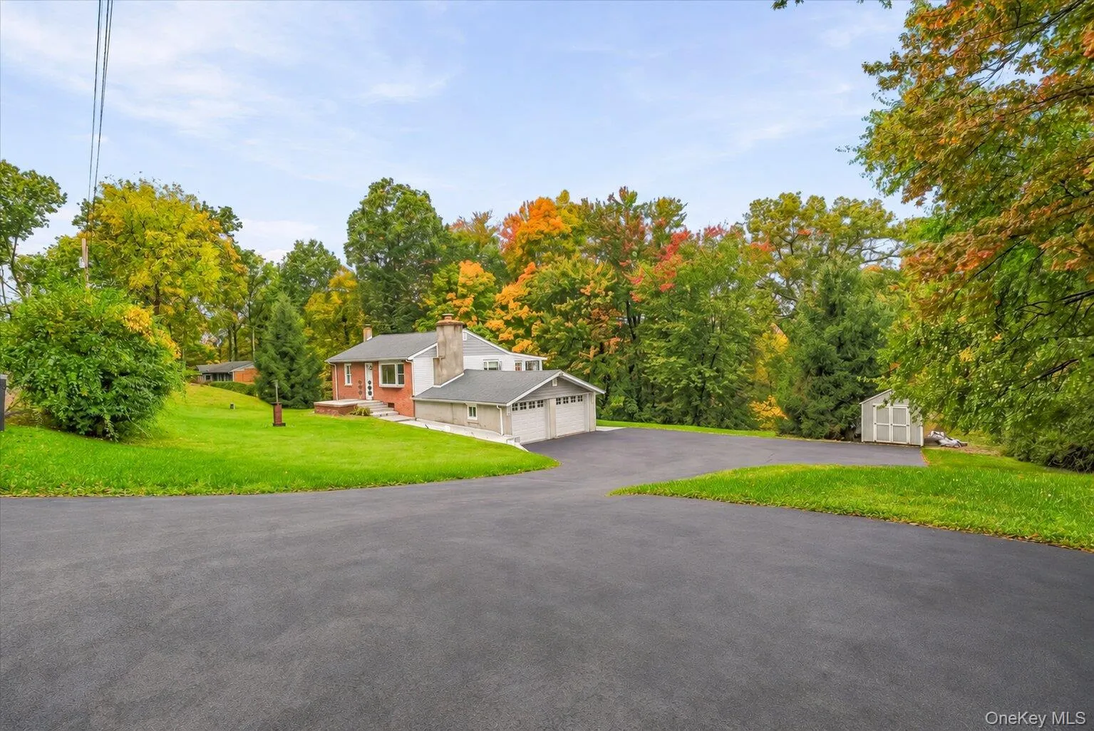 Wide exterior view showcasing the home with brick and siding accents, attached two-car garage, expansive paved driveway, green lawn, detached storage shed, and mature trees displaying beautiful autumn colors. Wide exterior view showcasing the home with brick and siding accents, attached two-car garage, expansive paved driveway, green lawn, detached storage shed, and mature trees displaying beautiful autumn colors.
