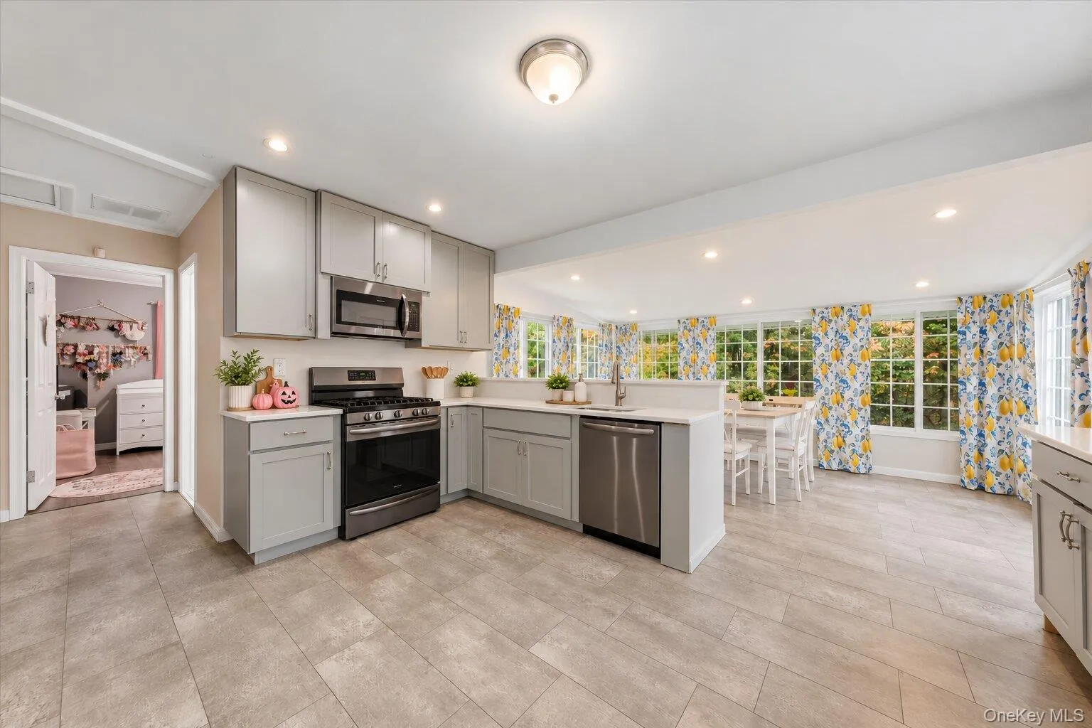 Virtually decluttered. Open kitchen featuring gray cabinetry, stainless steel appliances, tile flooring, and an adjoining dining area surrounded by windows. Virtually decluttered. Open kitchen featuring gray cabinetry, stainless steel appliances, tile flooring, and an adjoining dining area surrounded by windows.