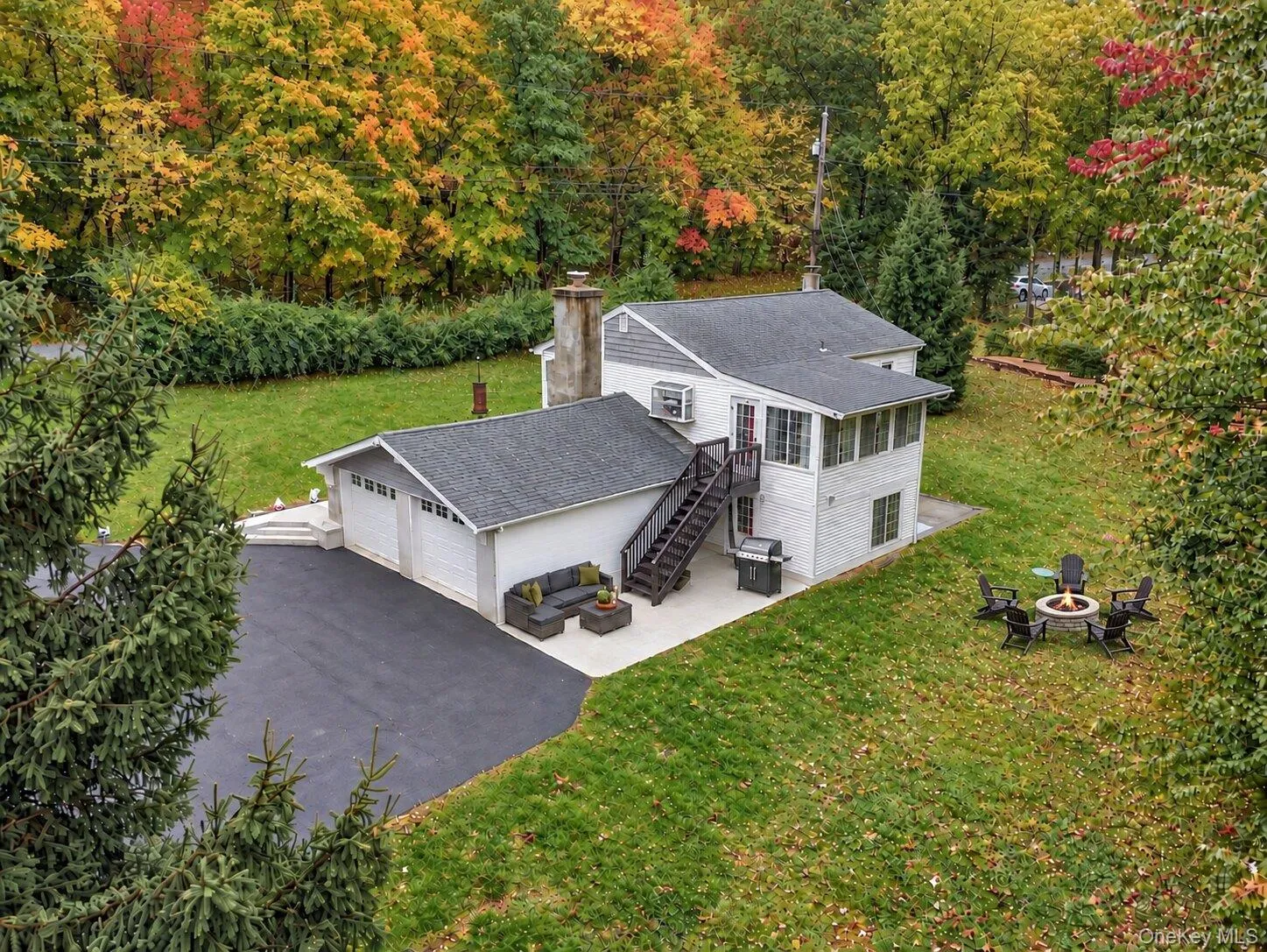 Aerial view showcasing the home, attached two-car garage, paved driveway, lawn areas, and mature trees surrounding the property. Aerial view showcasing the home, attached two-car garage, paved driveway, lawn areas, and mature trees surrounding the property.
