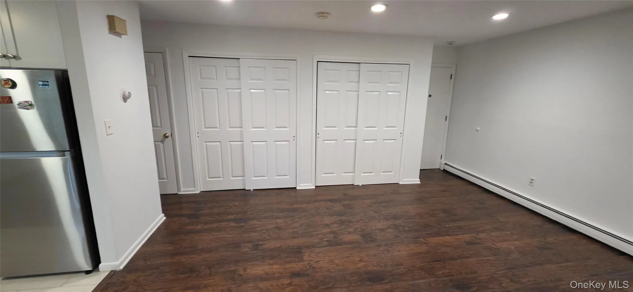 Wood-finish flooring, two sets of white bi-fold closet doors, recessed lighting, and white walls Wood-finish flooring, two sets of white bi-fold closet doors, recessed lighting, and white walls