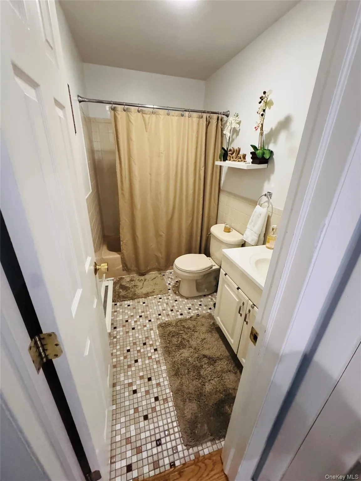 Bathroom featuring mosaic tile flooring, a white vanity with cabinet storage, and a built-in bathtub with tiled surround Bathroom featuring mosaic tile flooring, a white vanity with cabinet storage, and a built-in bathtub with tiled surround