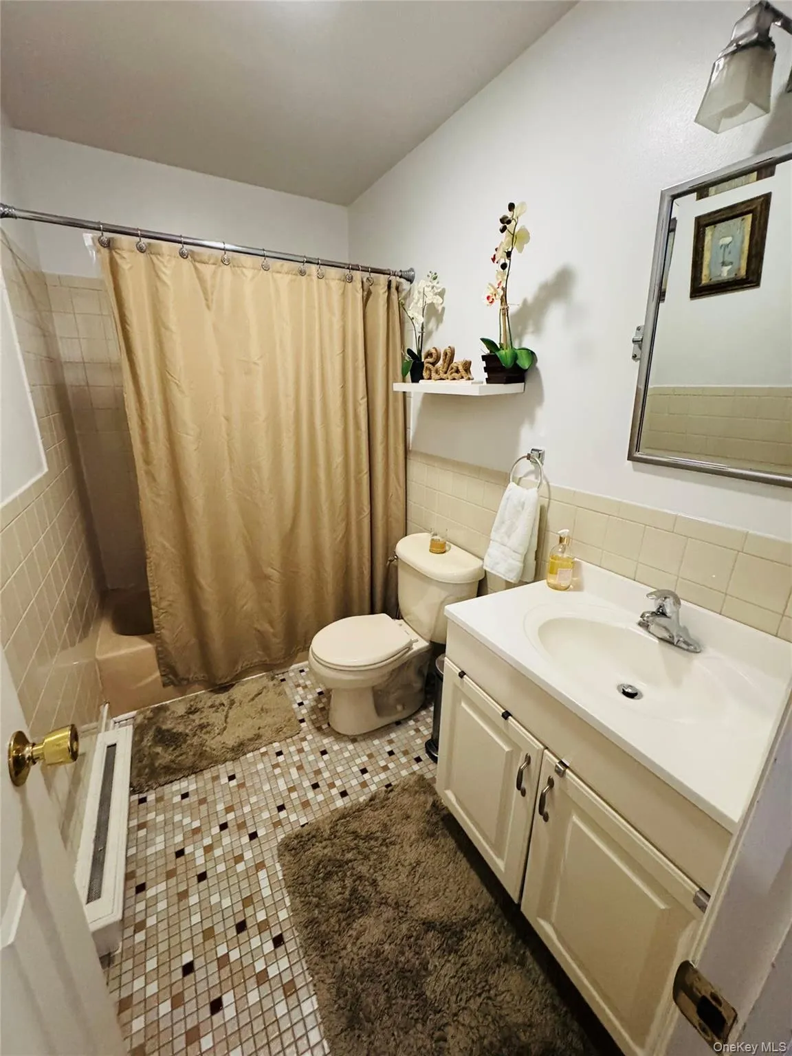 Mosaic tile flooring, single vanity with under-sink cabinetry, white countertop, and tiled shower surround Mosaic tile flooring, single vanity with under-sink cabinetry, white countertop, and tiled shower surround
