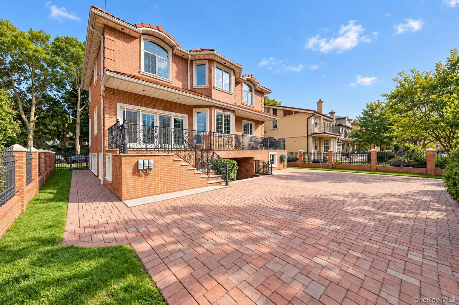 Brick exterior with a tile roof, featuring a paver driveway, wrought iron balcony, and a brick privacy wall with iron fencing Brick exterior with a tile roof, featuring a paver driveway, wrought iron balcony, and a brick privacy wall with iron fencing