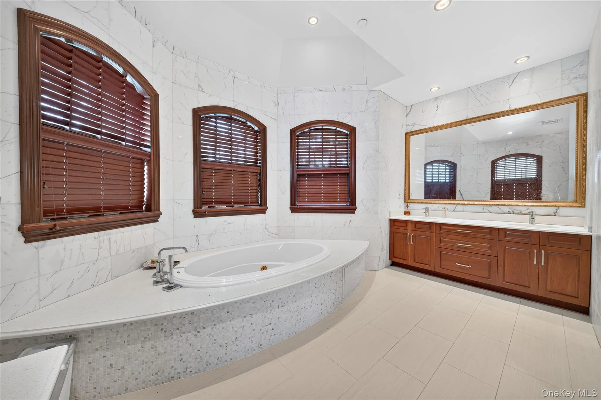 Integrated soaking tub with deck, dual vanities with undermount sinks, large wall mirror, and tiled walls Integrated soaking tub with deck, dual vanities with undermount sinks, large wall mirror, and tiled walls