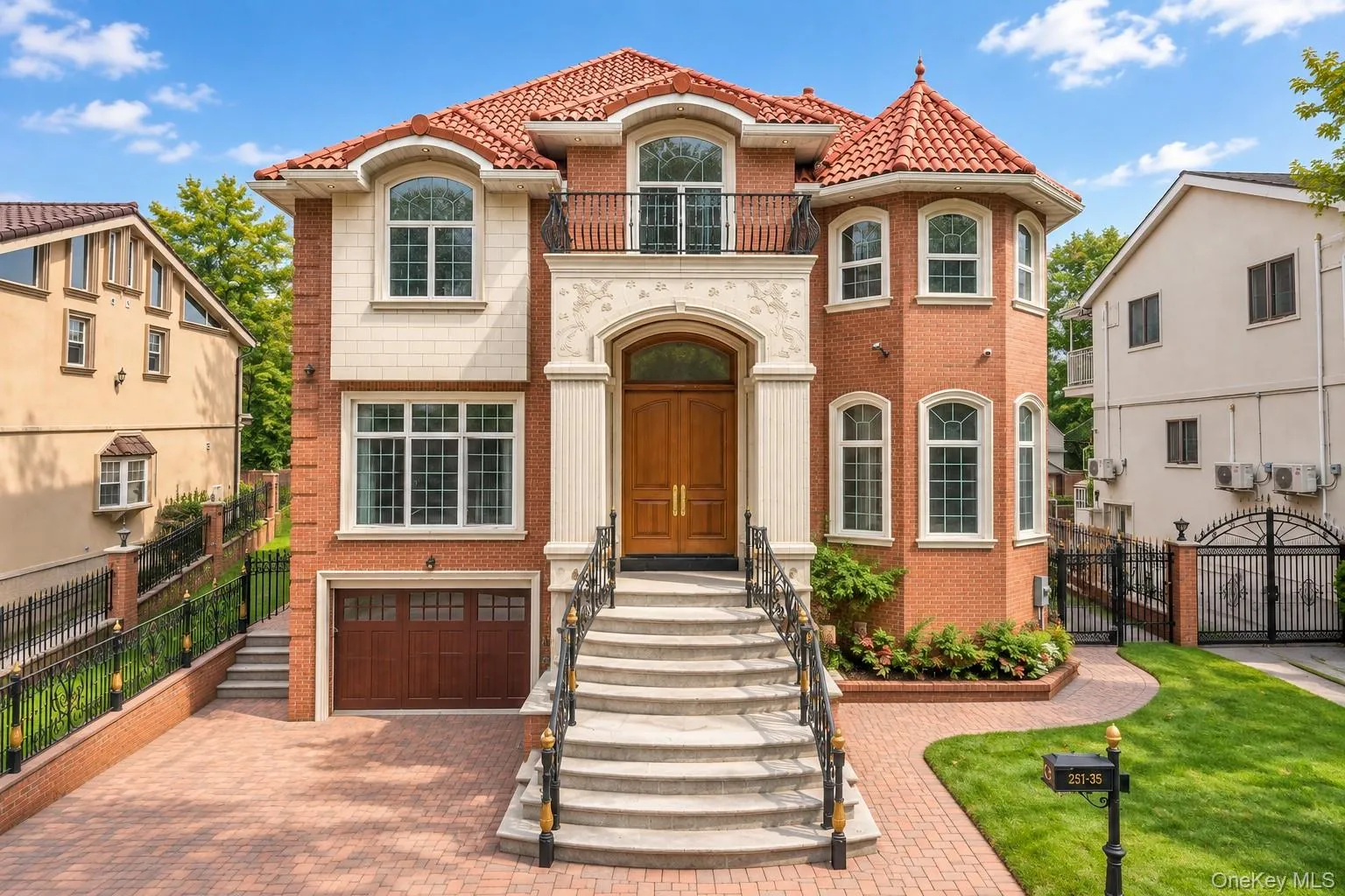 Red brick exterior with a terracotta tile roof, prominent arched entryway, a stone balustrade balcony, and a paved driveway with a garage door Red brick exterior with a terracotta tile roof, prominent arched entryway, a stone balustrade balcony, and a paved driveway with a garage door