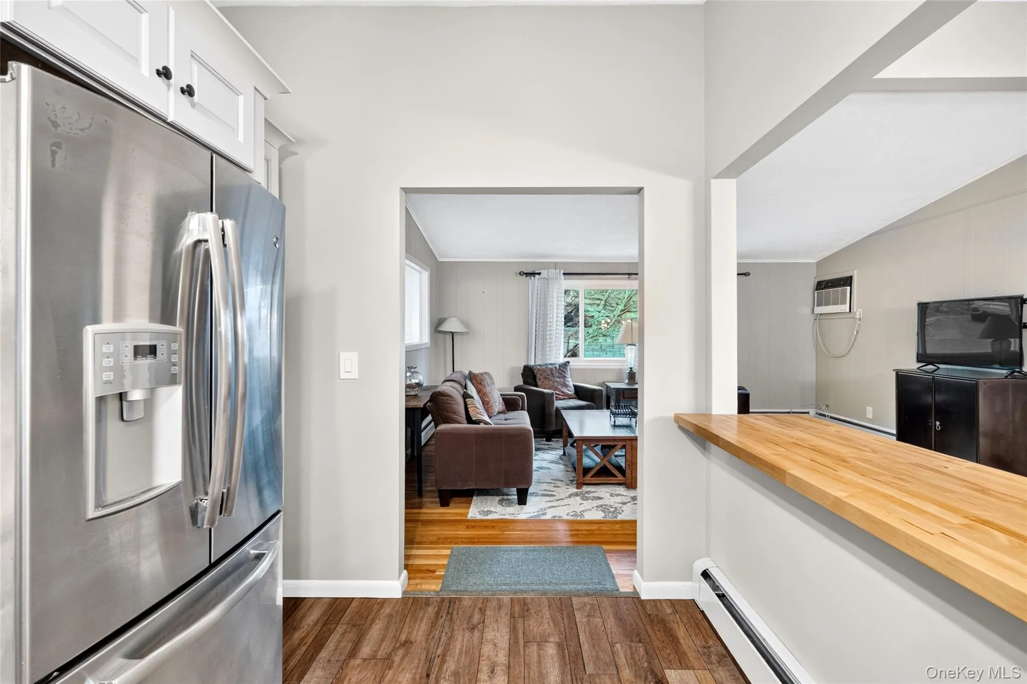 Stainless steel refrigerator with a built-in ice and water dispenser, white upper cabinetry, wood-finish flooring, and a natural wood-finish half-wall countertop Stainless steel refrigerator with a built-in ice and water dispenser, white upper cabinetry, wood-finish flooring, and a natural wood-finish half-wall countertop
