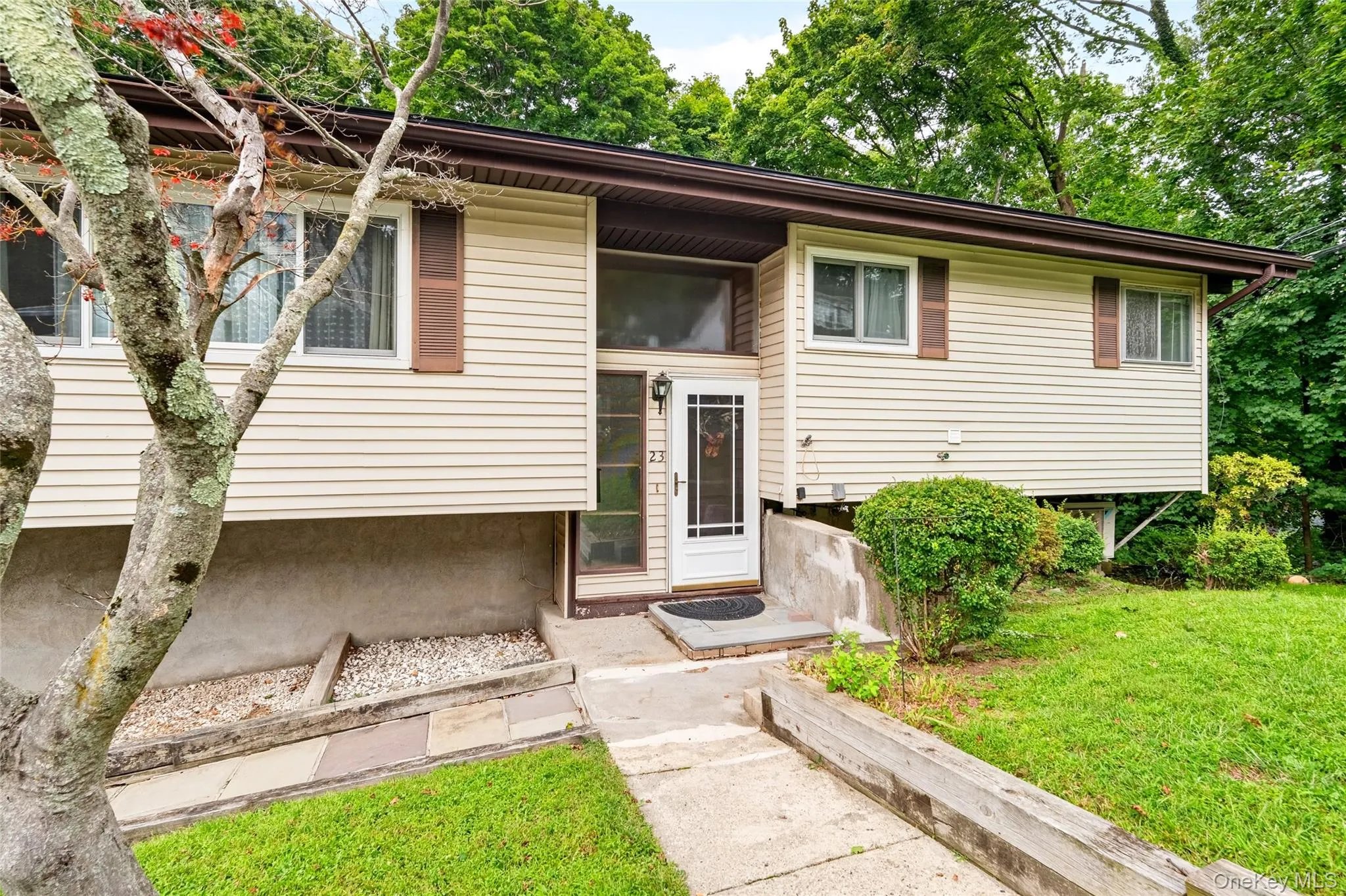 Cream-colored siding exterior, brown window shutters, white entry door with decorative glass, concrete walkway, and established landscaping Cream-colored siding exterior, brown window shutters, white entry door with decorative glass, concrete walkway, and established landscaping