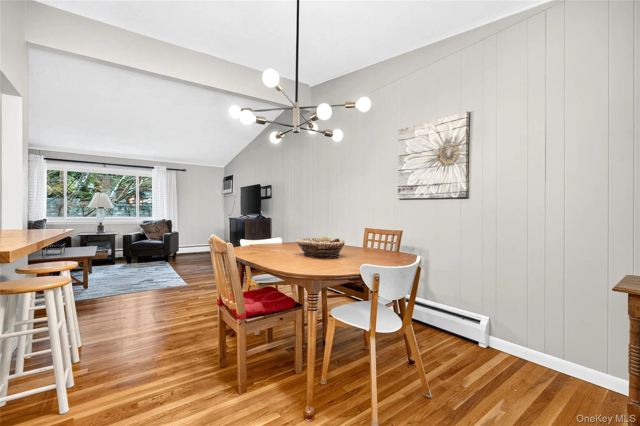 Vaulted ceiling with a modern chandelier, wood-finish flooring, and light-colored paneled walls Vaulted ceiling with a modern chandelier, wood-finish flooring, and light-colored paneled walls