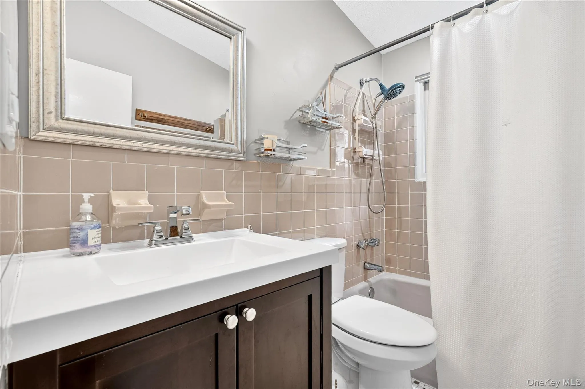 Full bathroom featuring a vanity with a white countertop, chrome faucet, a framed mirror, and a tiled shower/tub combination Full bathroom featuring a vanity with a white countertop, chrome faucet, a framed mirror, and a tiled shower/tub combination