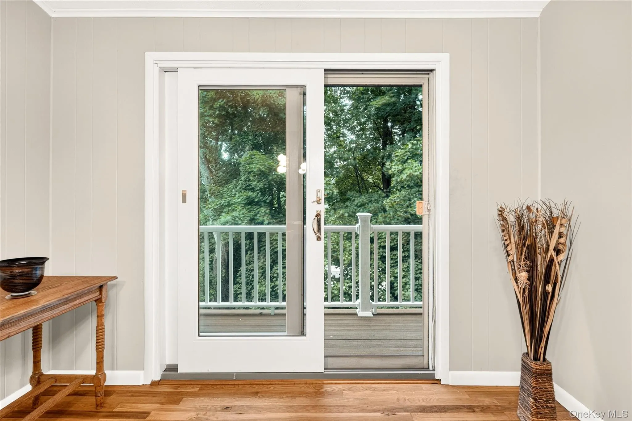 Wood-finish flooring, vertical paneling, crown molding, and sliding glass doors with direct outdoor access Wood-finish flooring, vertical paneling, crown molding, and sliding glass doors with direct outdoor access