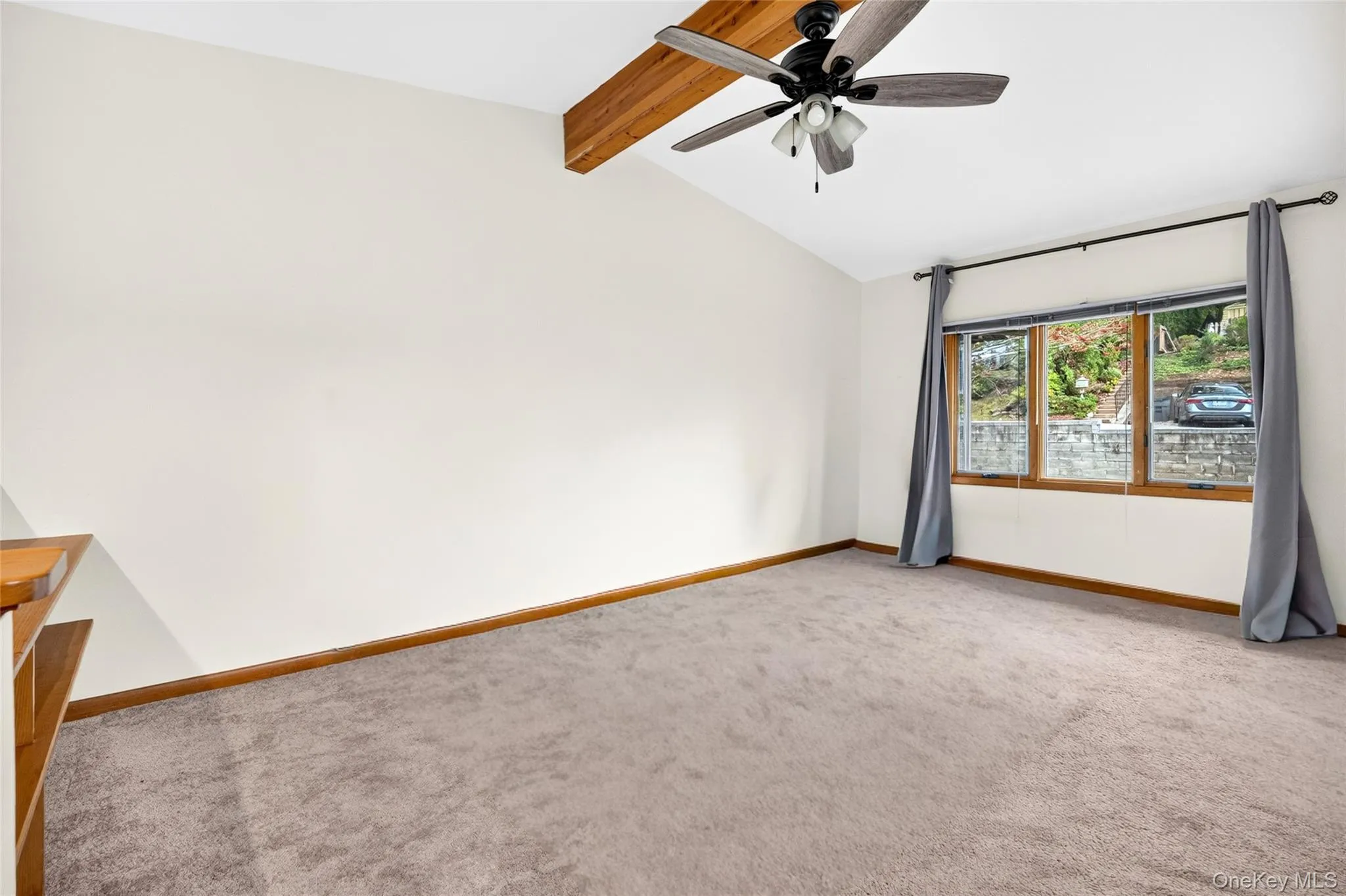 Vaulted ceiling with exposed wood beam, ceiling fan, and carpeted flooring Vaulted ceiling with exposed wood beam, ceiling fan, and carpeted flooring